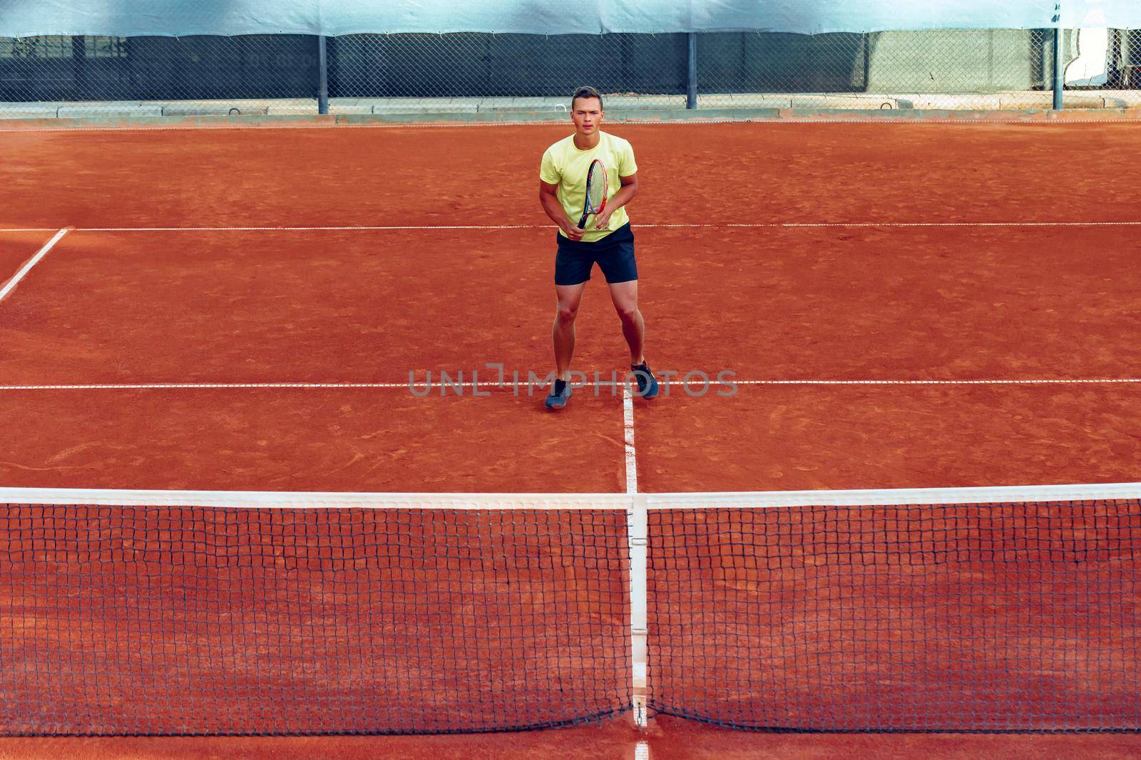 Young handsome man playing tennis on the clay tennis court