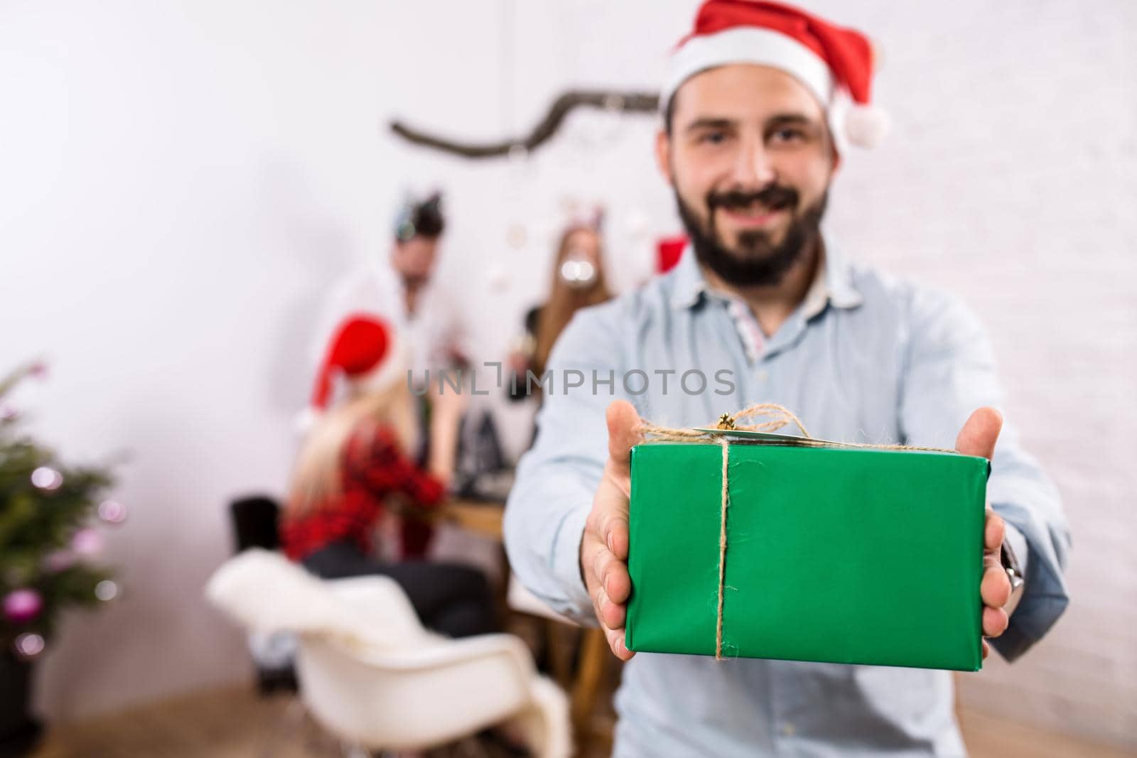 Shot of happy friends enjoying holidays. Focus on the man in the foreground in a red Christmas hat by nazarovsergey