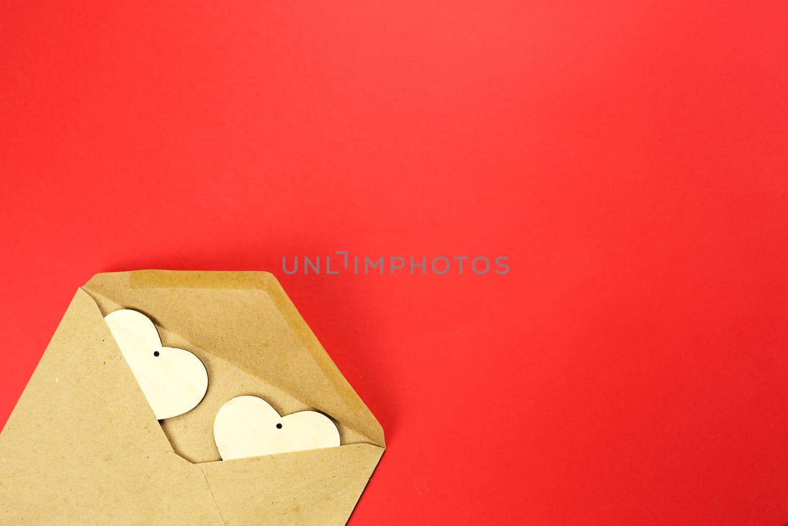 Wooden hearts spill out of an open envelope on a red background. Valentine's Day, love letter, declaration of love, acquaintance. Copy space, mock up