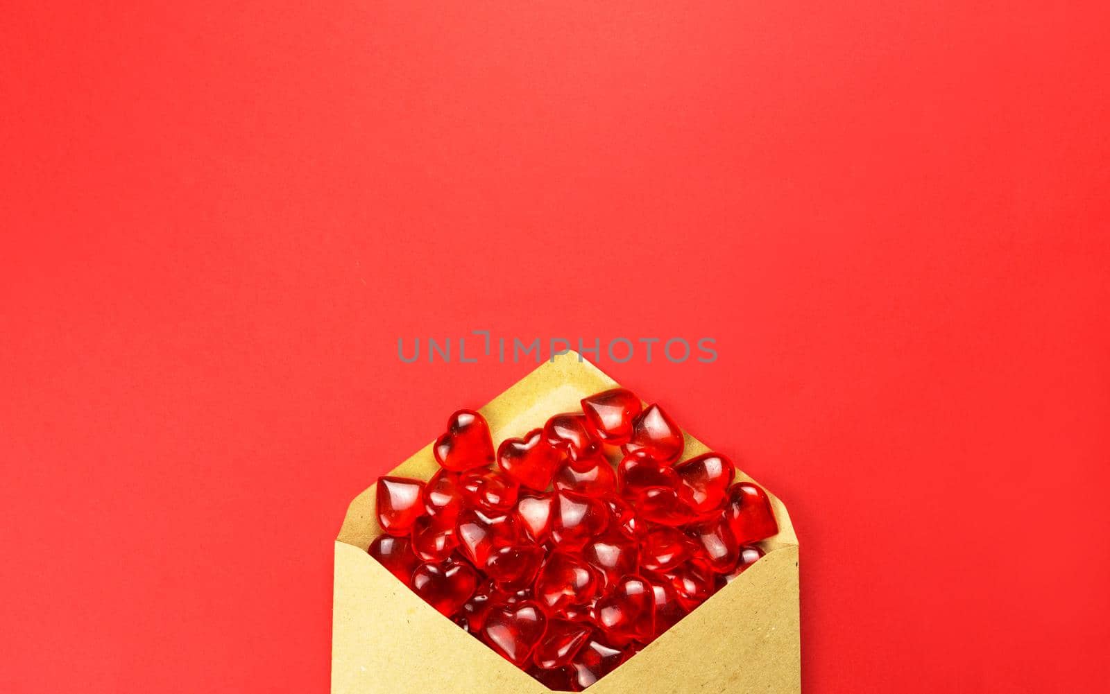 Glass hearts spill out of an open envelope on a red background. Valentine's Day, love letter, declaration of love, acquaintance. Copy space, mock up by Simol