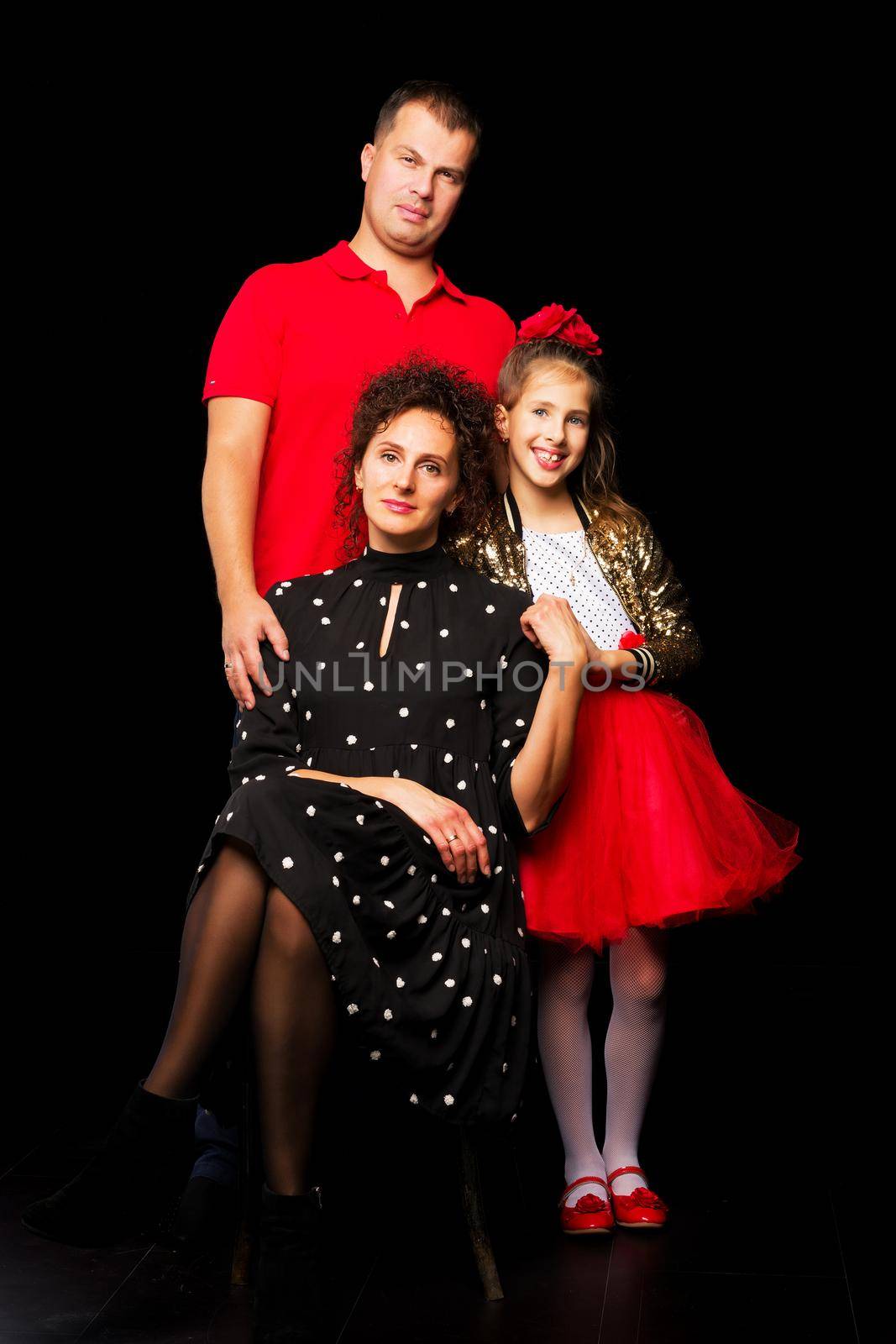 Family portrait, mom and dad with a charming little daughter. On a black background. The concept of family happiness.