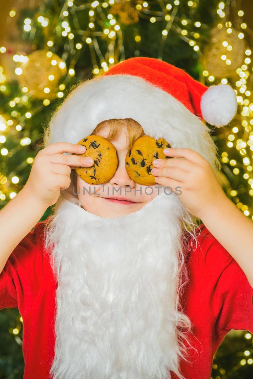 Santa funny child picking cookie. Little Santa holding Christmas cookies against eyes. by Tverdokhlib