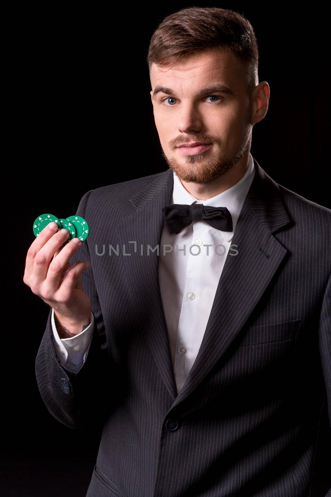 man in a suit posing with chips for gambling on black background