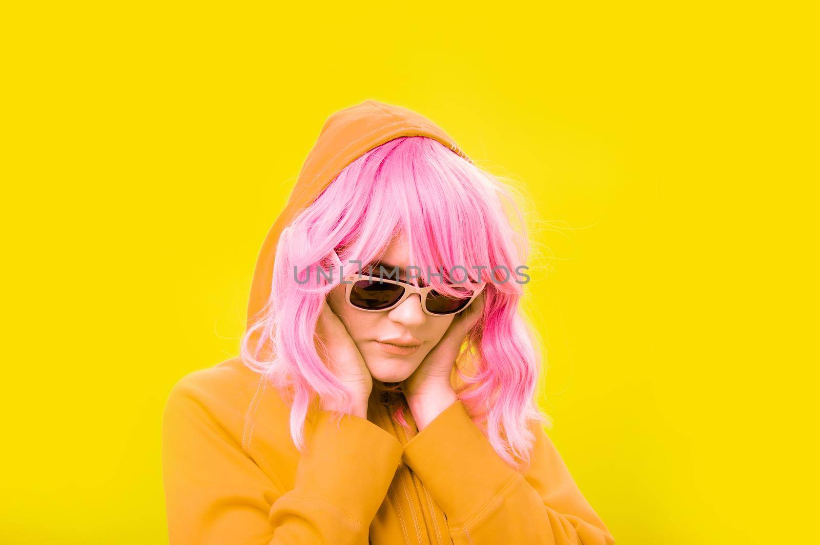 Alternative funky girl with pink hair on yellow background. Close up fashion portrait young beautiful woman in hoodie and glasses. Unusual youth fashion concept. Hot image.