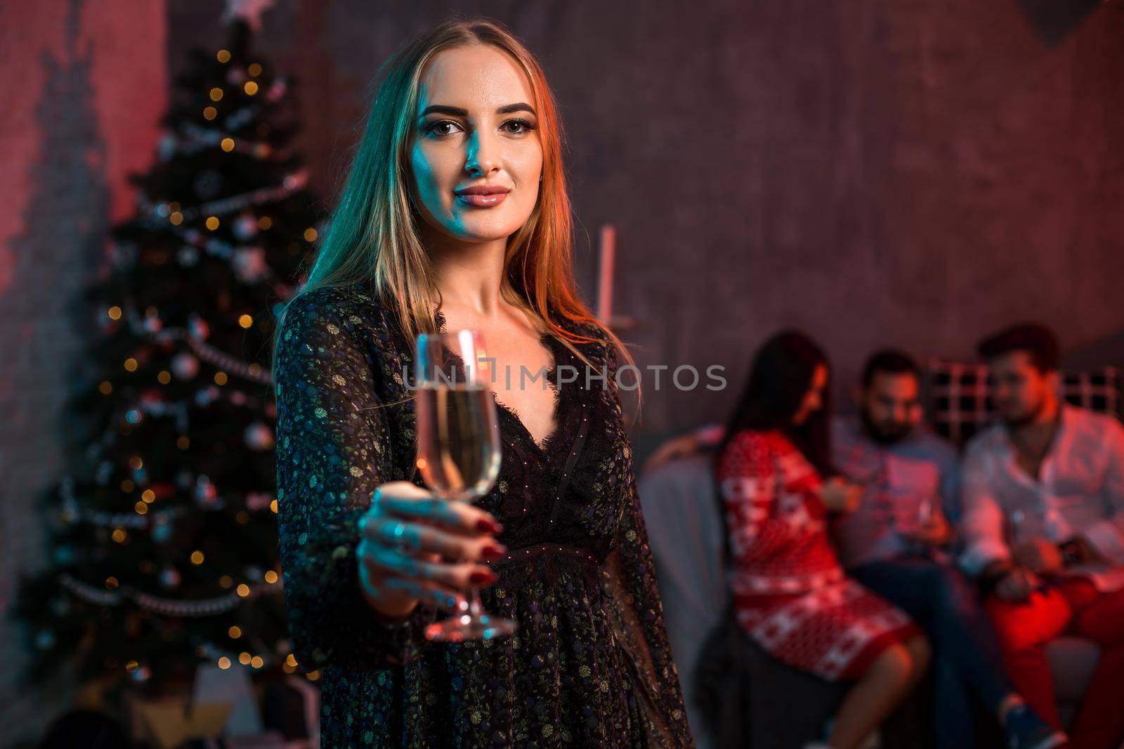 Beautiful young woman with glass of champagne at Christmas party. Funny people.