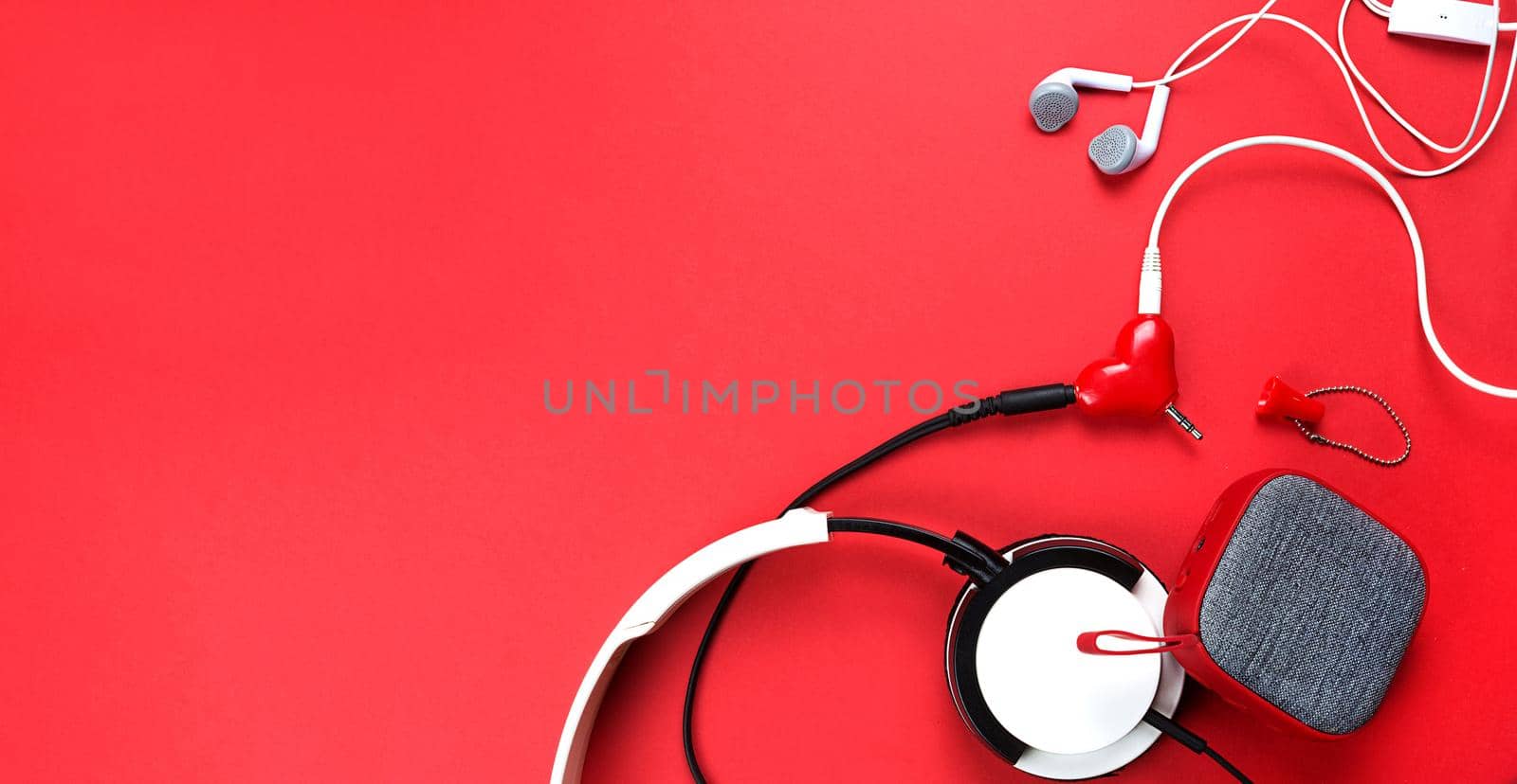 A heart-shaped headphone splitter for a couple in love. Connected to a red portable speaker and two pairs of headphones - flat lay. Valentine's day, love, modern technology, copy space by Simol