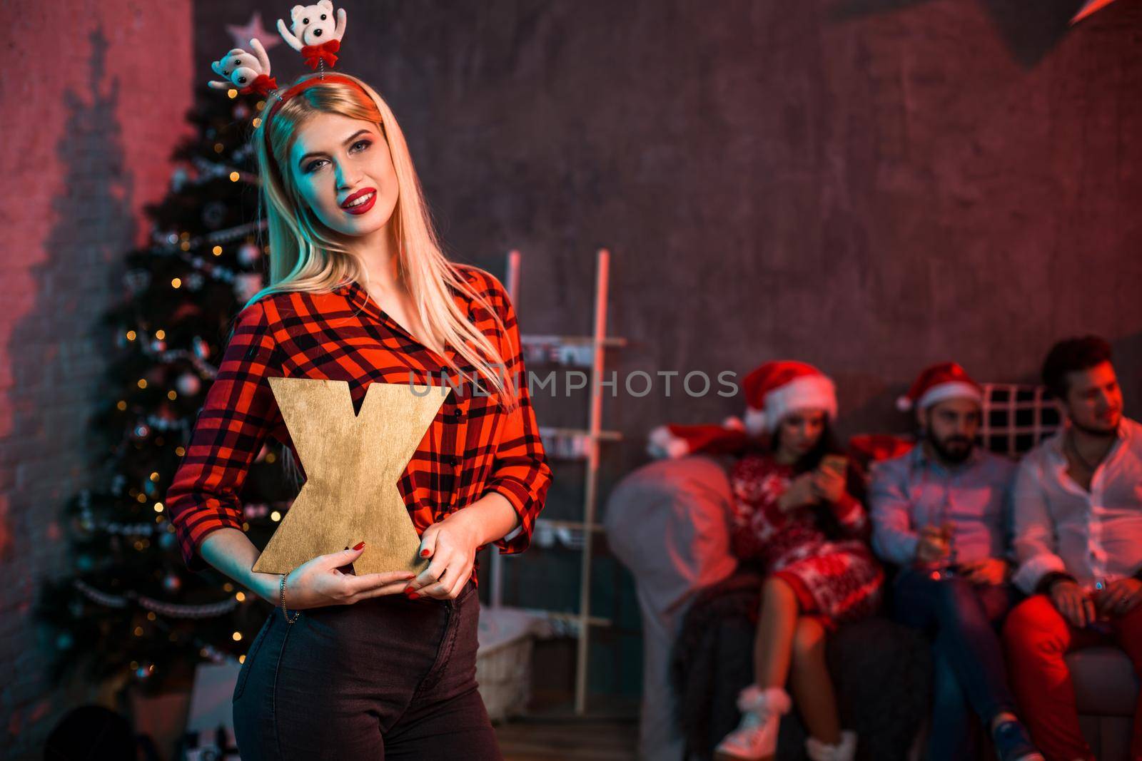 Christmas, x-mas, New year, winter, happiness concept - smiling woman in santa helper hat with a wooden letter X. Funny people. Christmas party at home