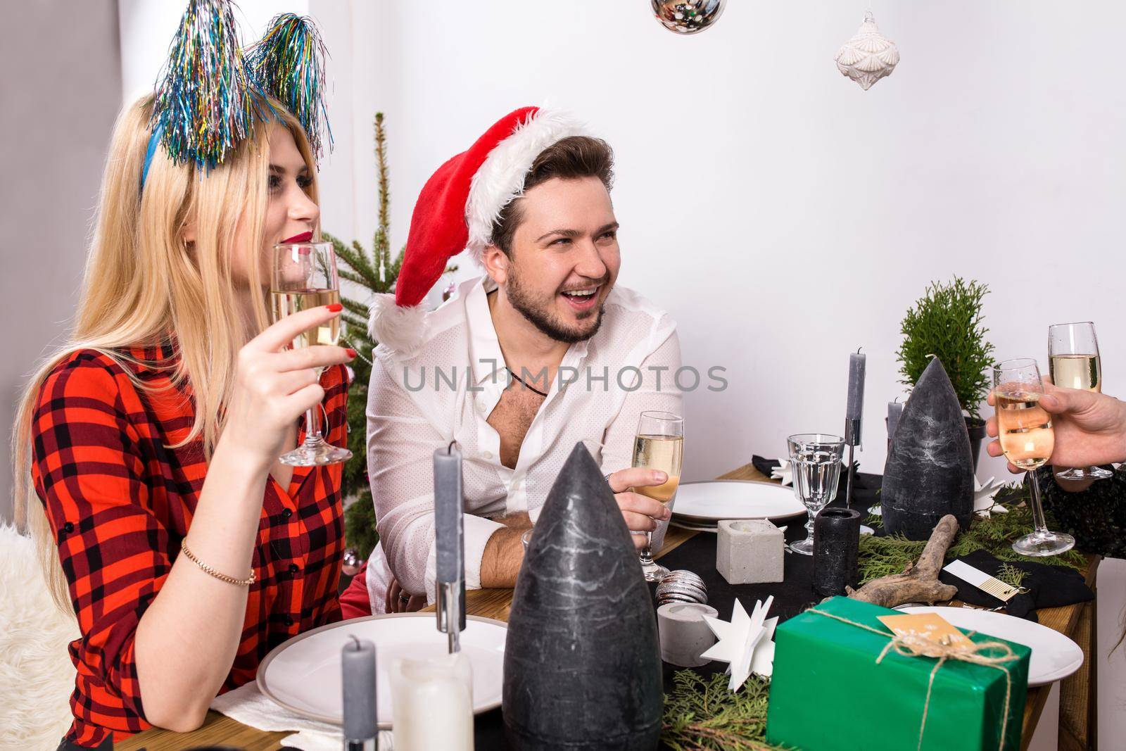 Christmas party cheerful friends at having drink and fun. Men and women at a festive table with glasses of champagne in a white room