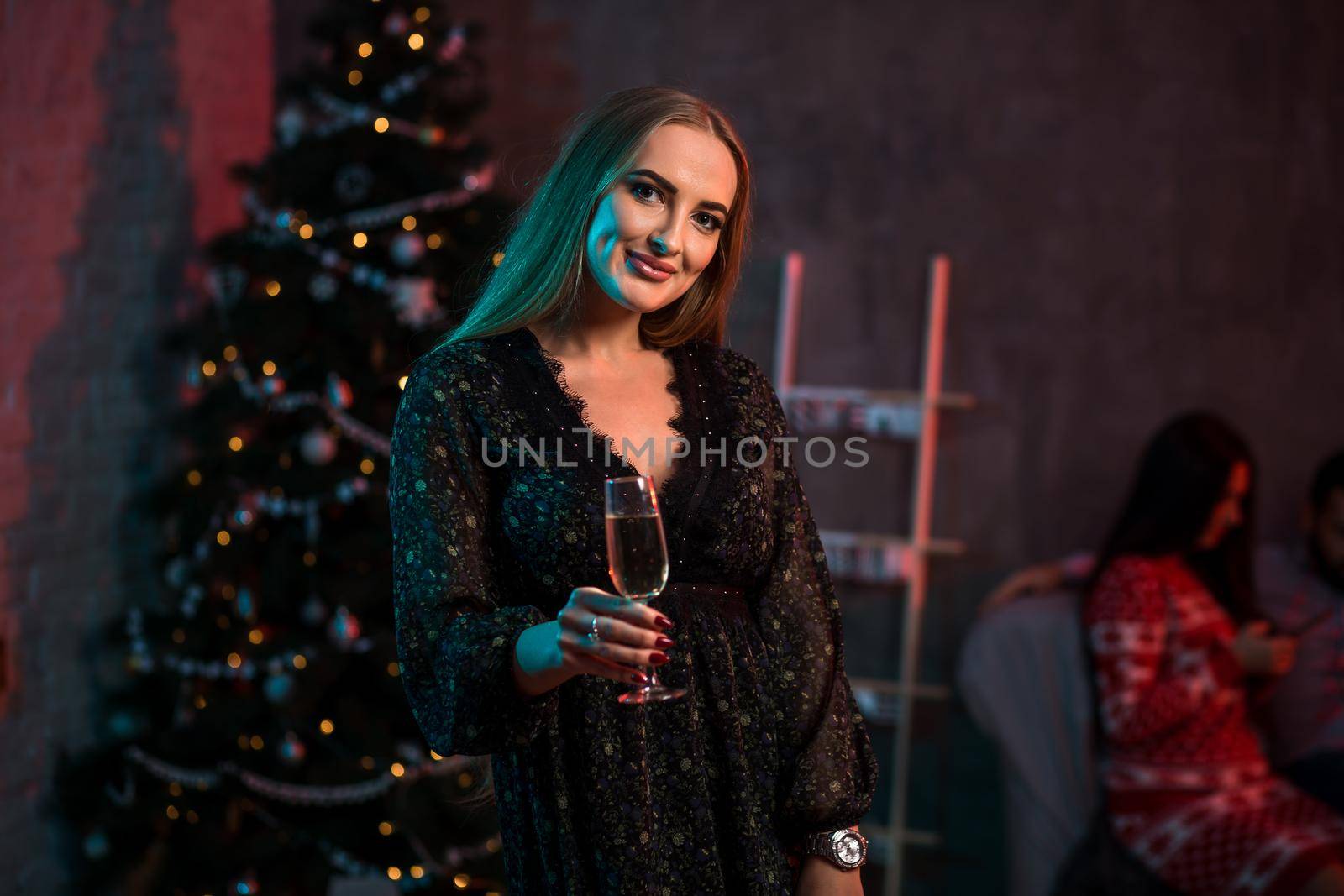 Beautiful young woman with glass of champagne at Christmas party. Funny people.