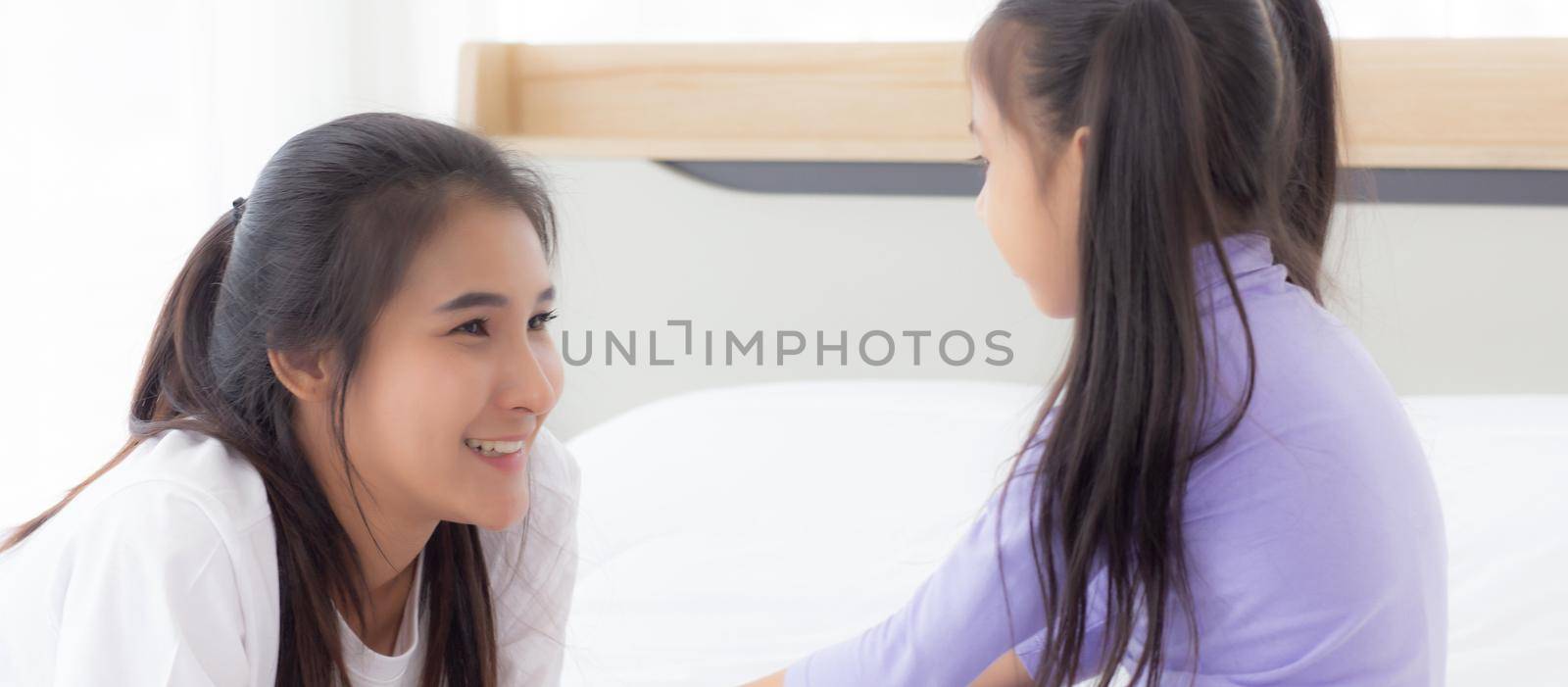 Young asian mom and daughter smiling and eye contact together with care in room, face of mother and girl looking eye with relationship and bonding, emotion and expression, family and love concept.