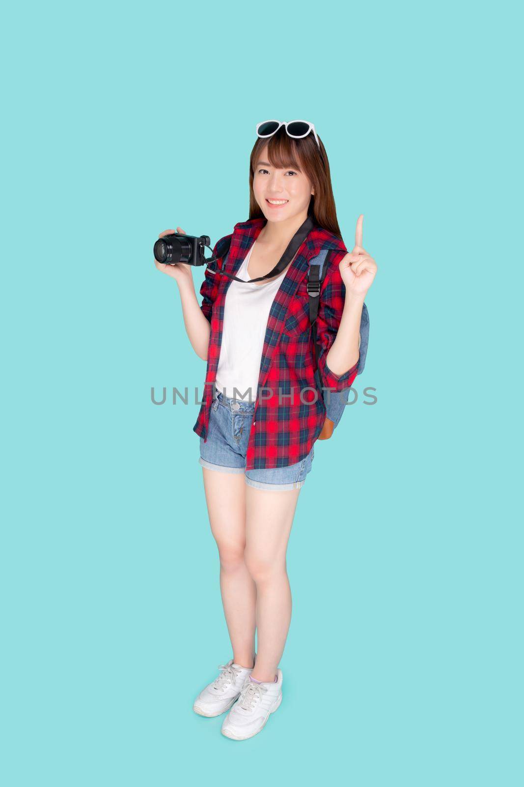 Beautiful young asian woman presenting travel trip summer with pointing something isolated on blue background, girl having activity hobby take a photo holding camera, journey in vacation and holiday.