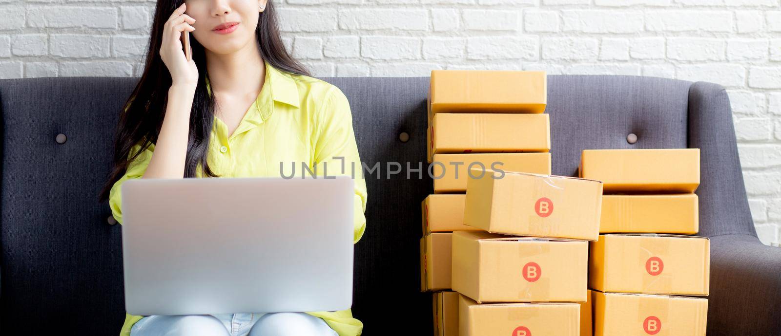 Young asian woman is entrepreneur talking with customer and using laptop computer while order purchase online at home, logistic and delivery, online shopping, female is seller of business SME.