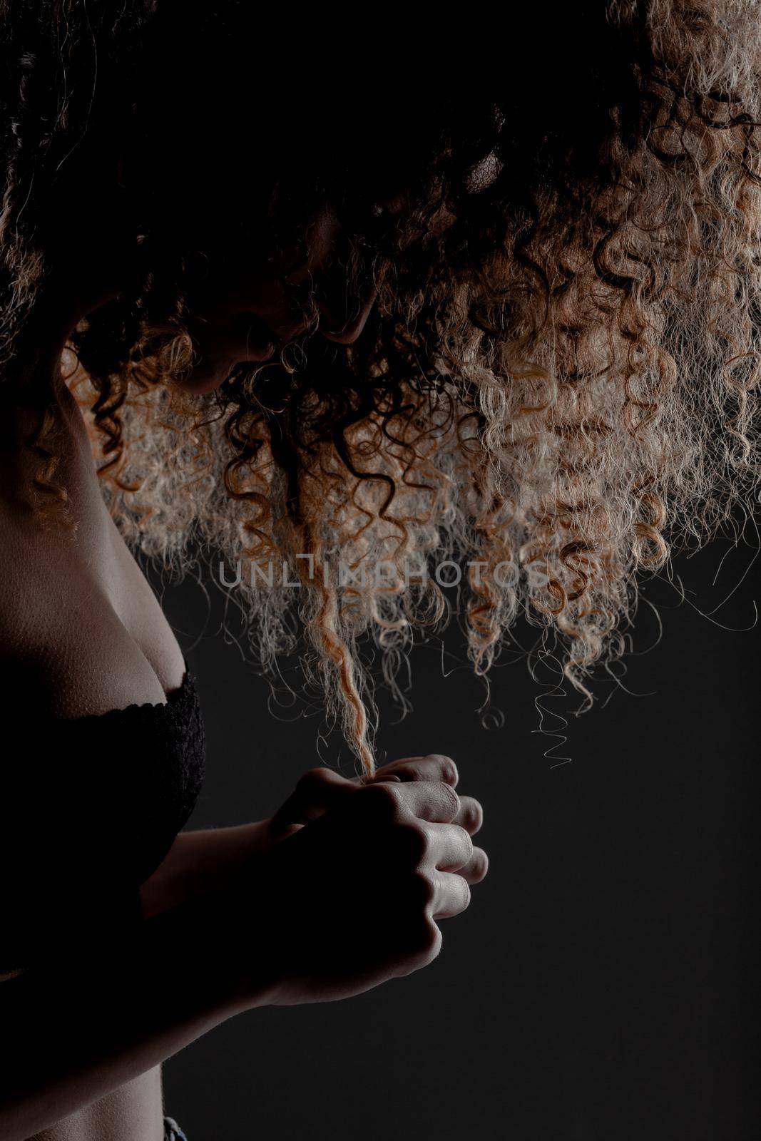 Side lit brunette girl with long curly hair, silhouette studio portrait on gray background.
