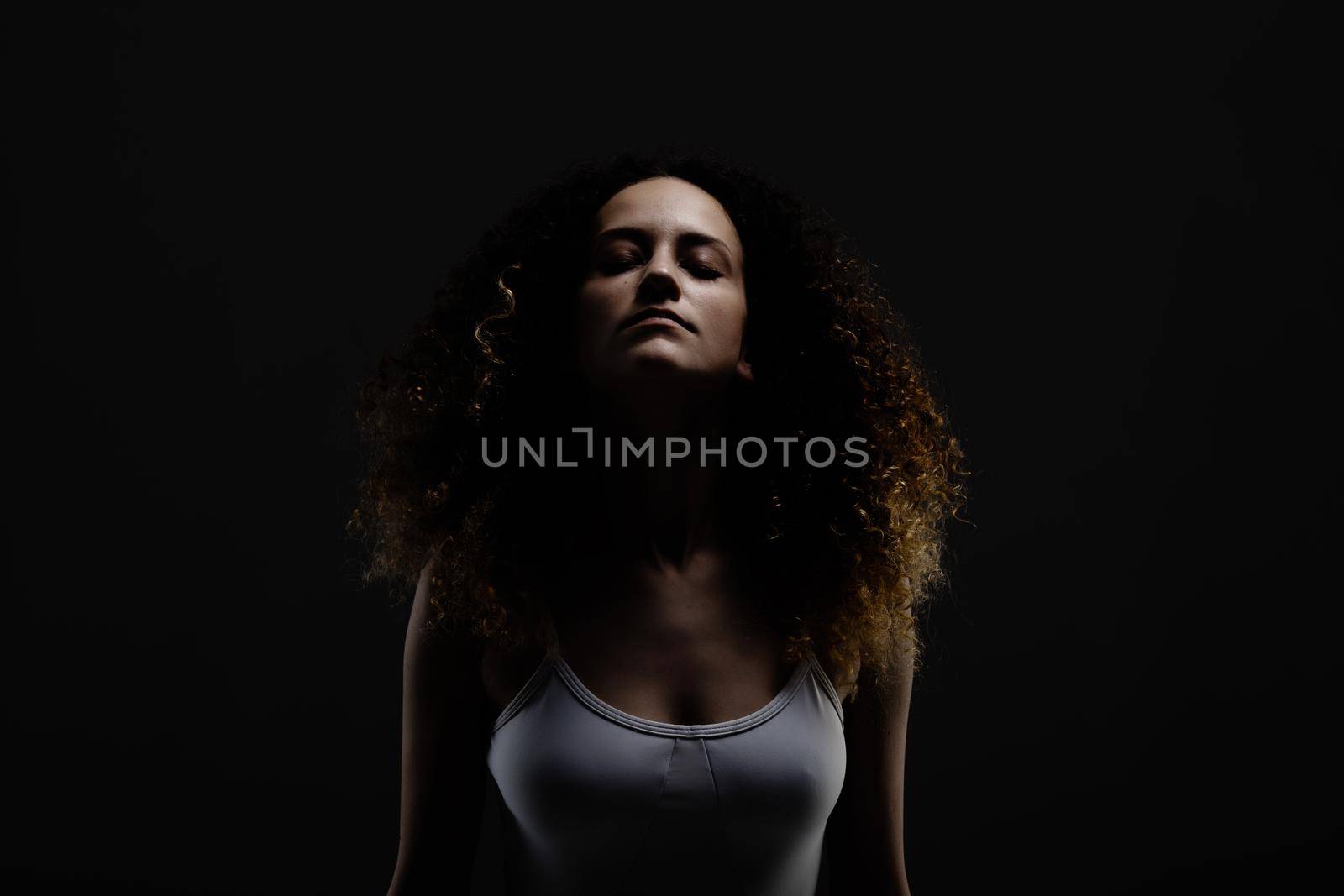 Beautiful girl with long curly hair. Dark portrait with closed eyes.