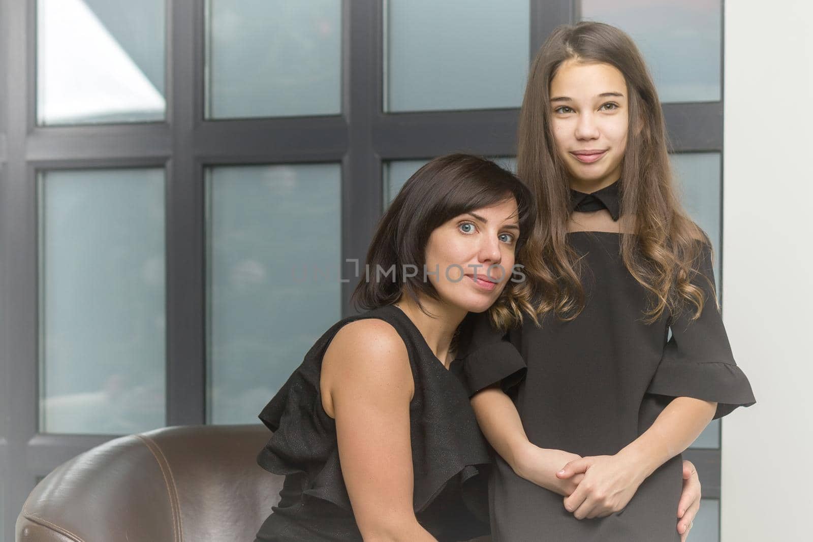 Happy family, mom and daughter near a large panoramic window, in the studio.