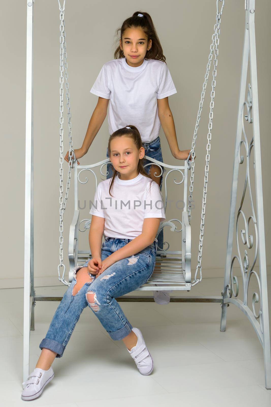 Two beautiful little girls near the swing. The concept of tenderness and beauty.