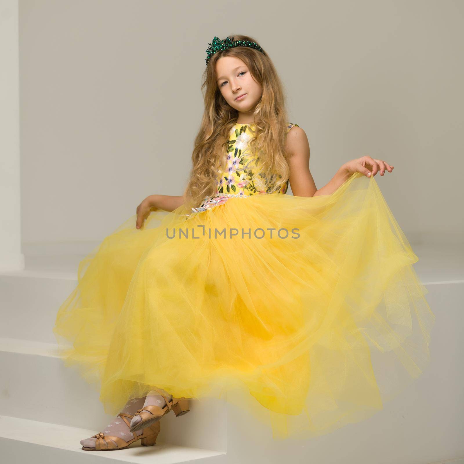 Beautiful little girl is sitting in the studio on a white staircase. Style and fashion concept, happy childhood.