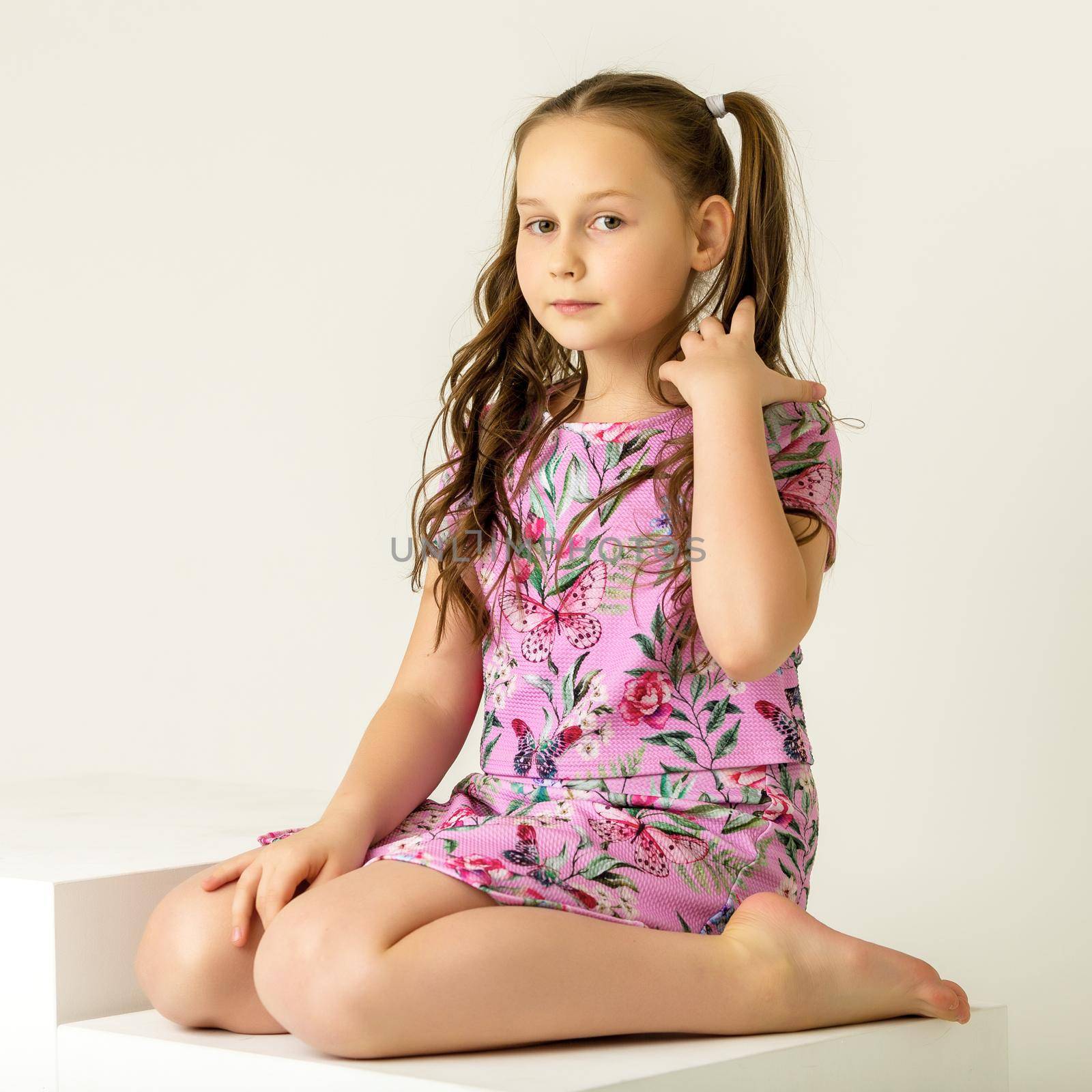 Beautiful little girl is sitting in the studio on a white staircase. Style and fashion concept, happy childhood.