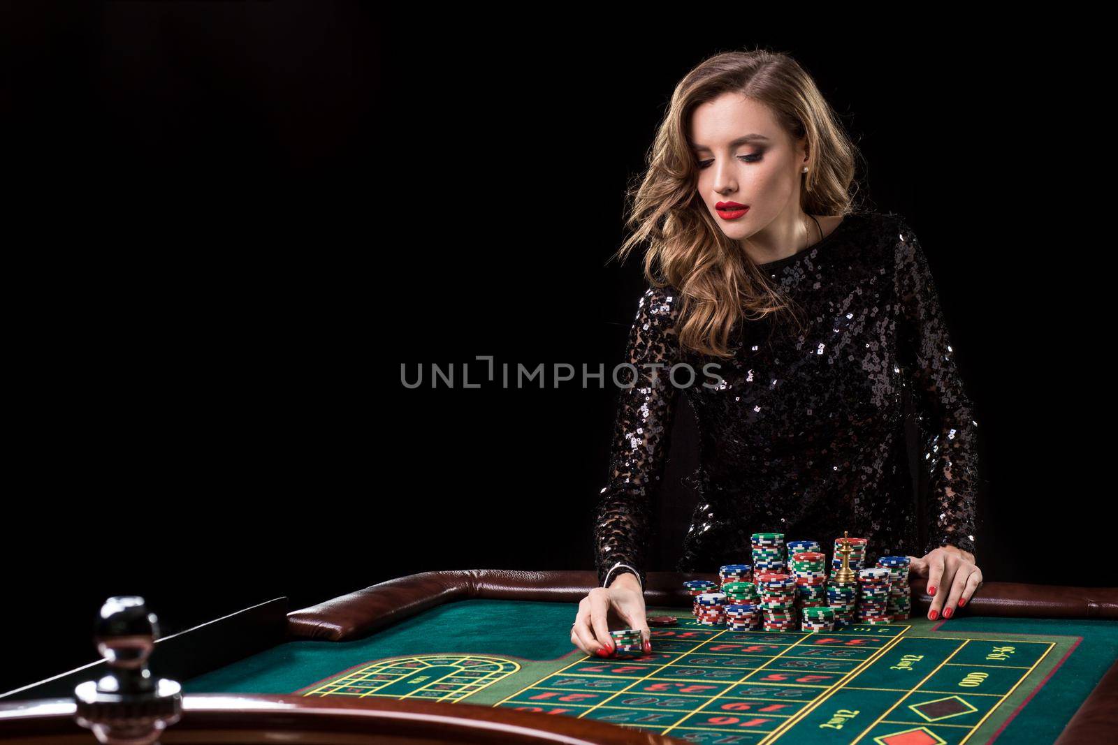 Sexy woman in a black dress playing in casino. Woman stakes piles of chips playing roulette at the casino club. Gambling. Roulette.