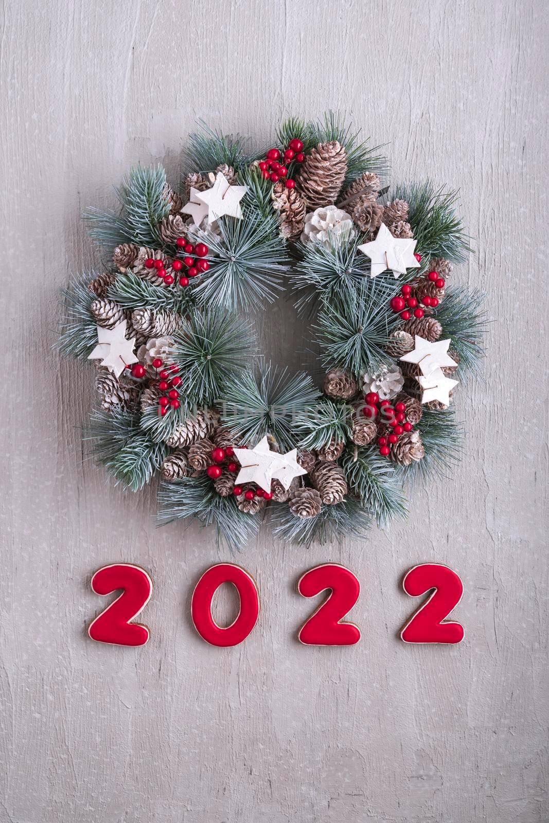 New Year decor with numbers 2022. Christmas wreath. Winter Holiday pattern. Light gray wall on background. Vertical frame.