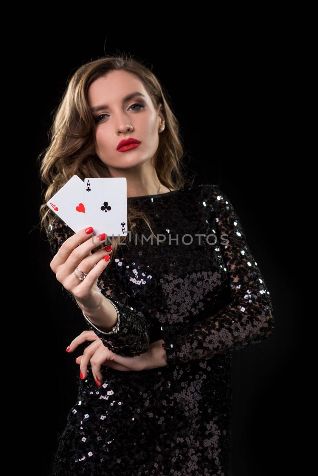 Young beautiful woman in black shiny dress holds poker cards in hands against a black background. The concept of gambling. Casino