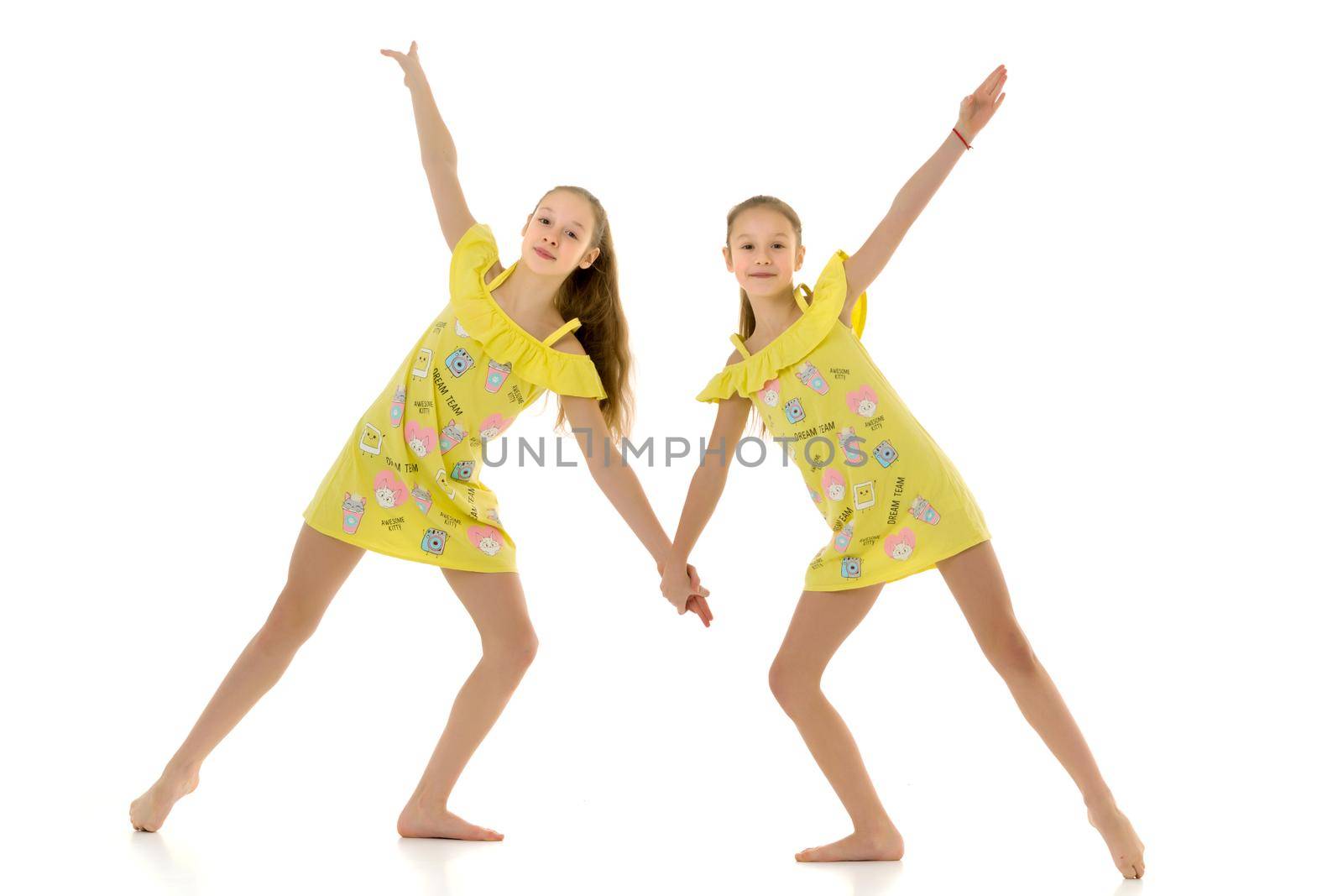 Cute Teen Girls Standing Together and Holding Hands, Two Barefoot Sisters Wearing Yellow Short Summer Dresses Smiling at Camera, Full Length Portrait of Cheerful Teenagers Isolated on White Background.