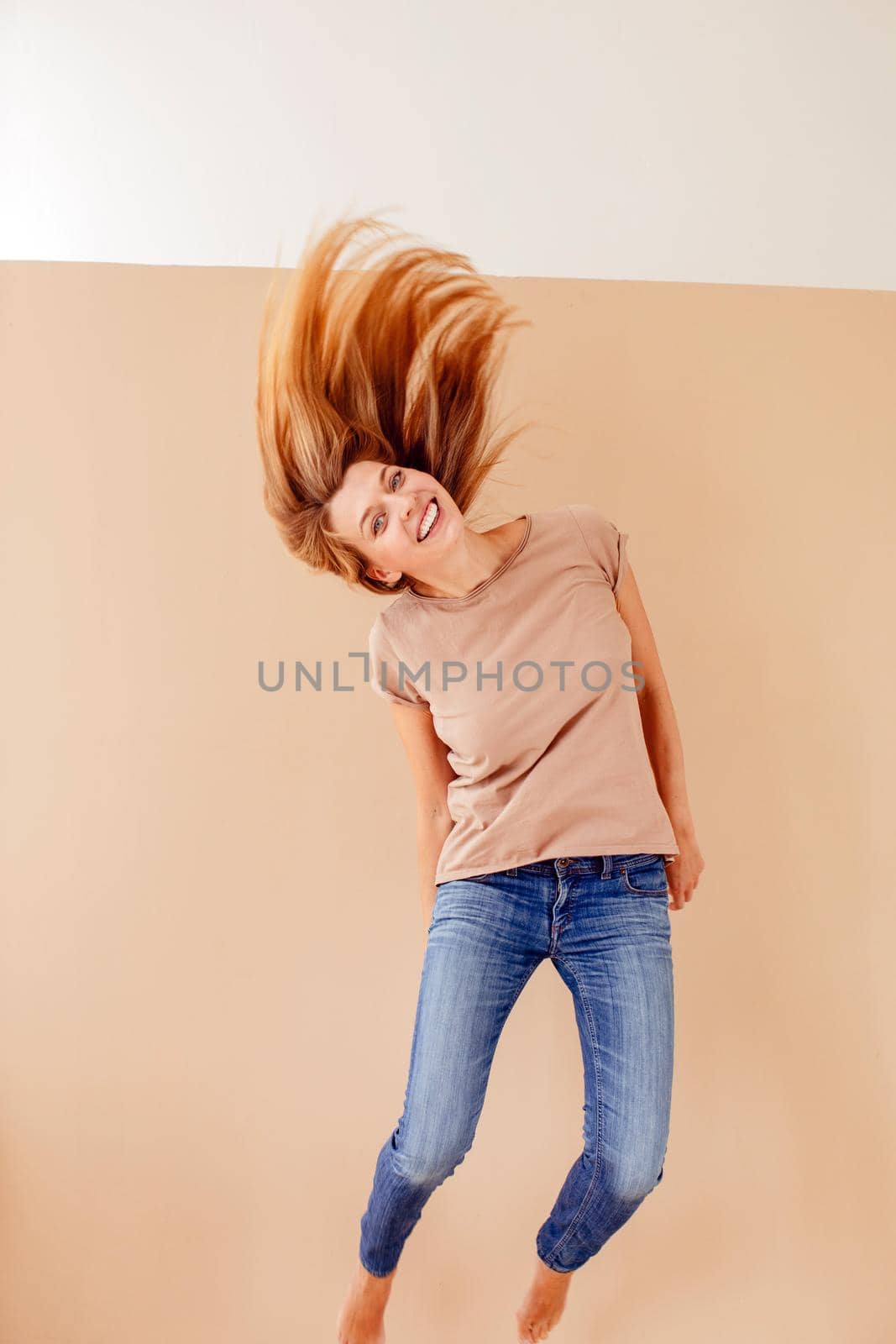Full length portrait of a joyful young woman jumping and celebrating over cream background