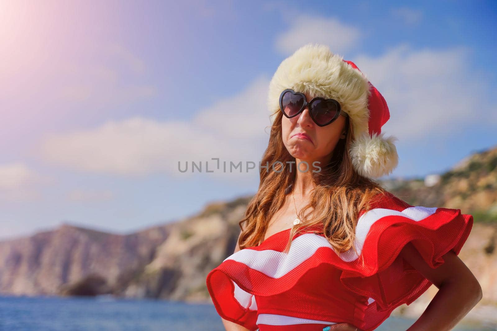 Young brunette woman in red swimsuit and Santa hat, swimming on kayak around basalt rocks like in Iceland. Back view. Christmas and travel concept