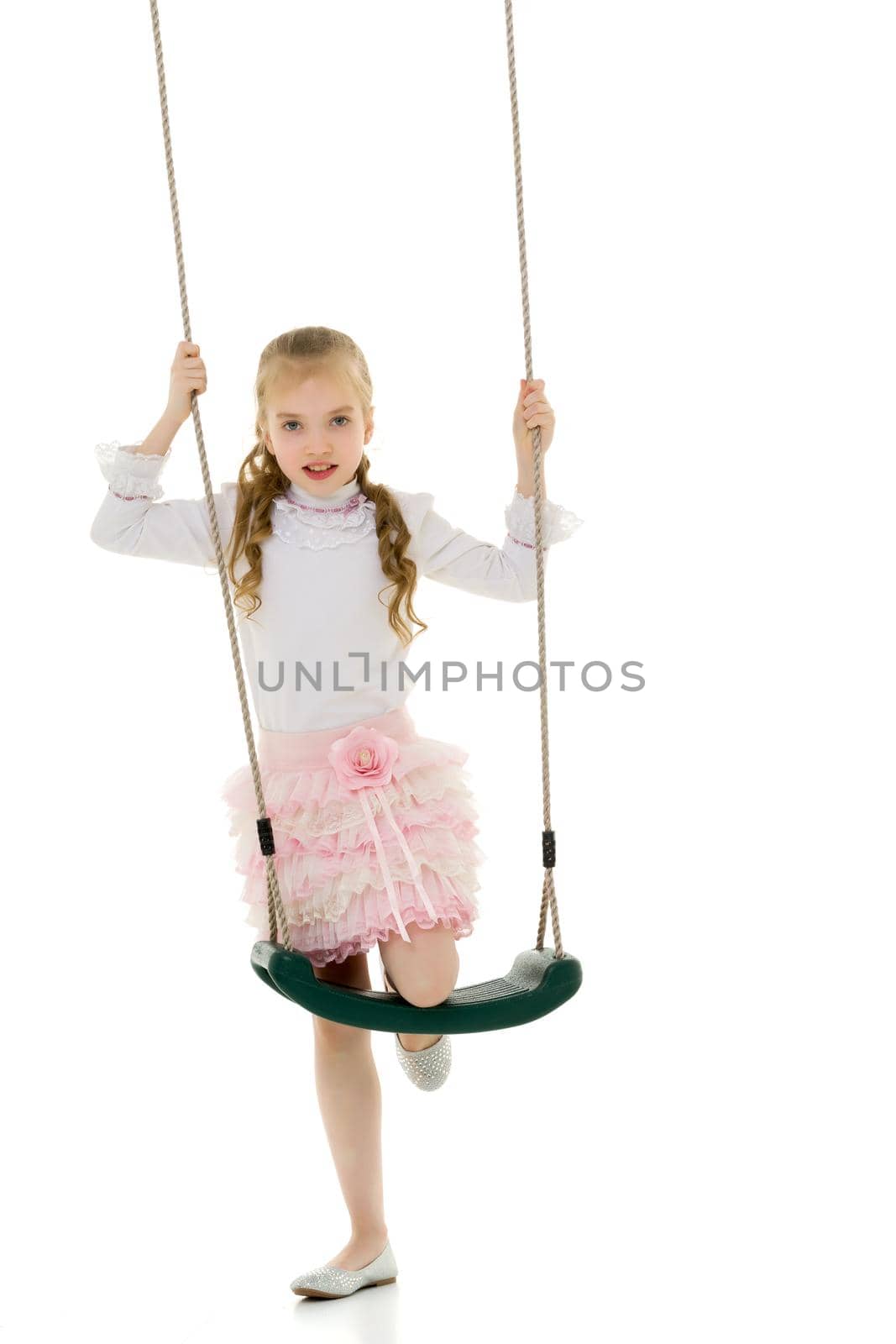 Beautiful little girl swinging in the studio on a swing. Concept of a happy childhood, family well-being.