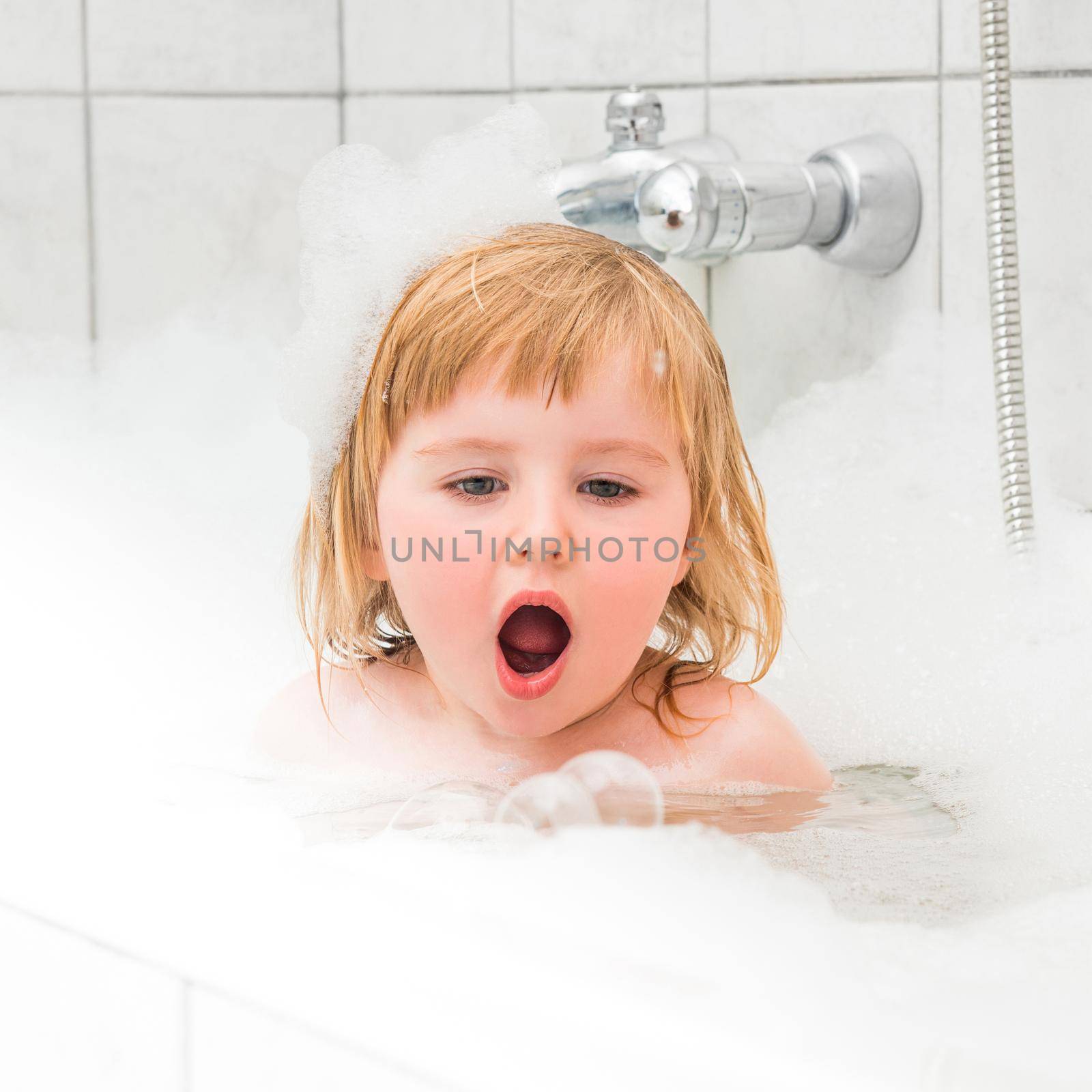 cute two year old baby bathes in a bath with foam closeup