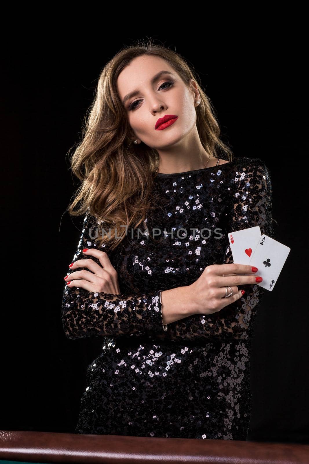 Young beautiful woman in black shiny dress holds poker cards in hands against a black background. The concept of gambling. Casino