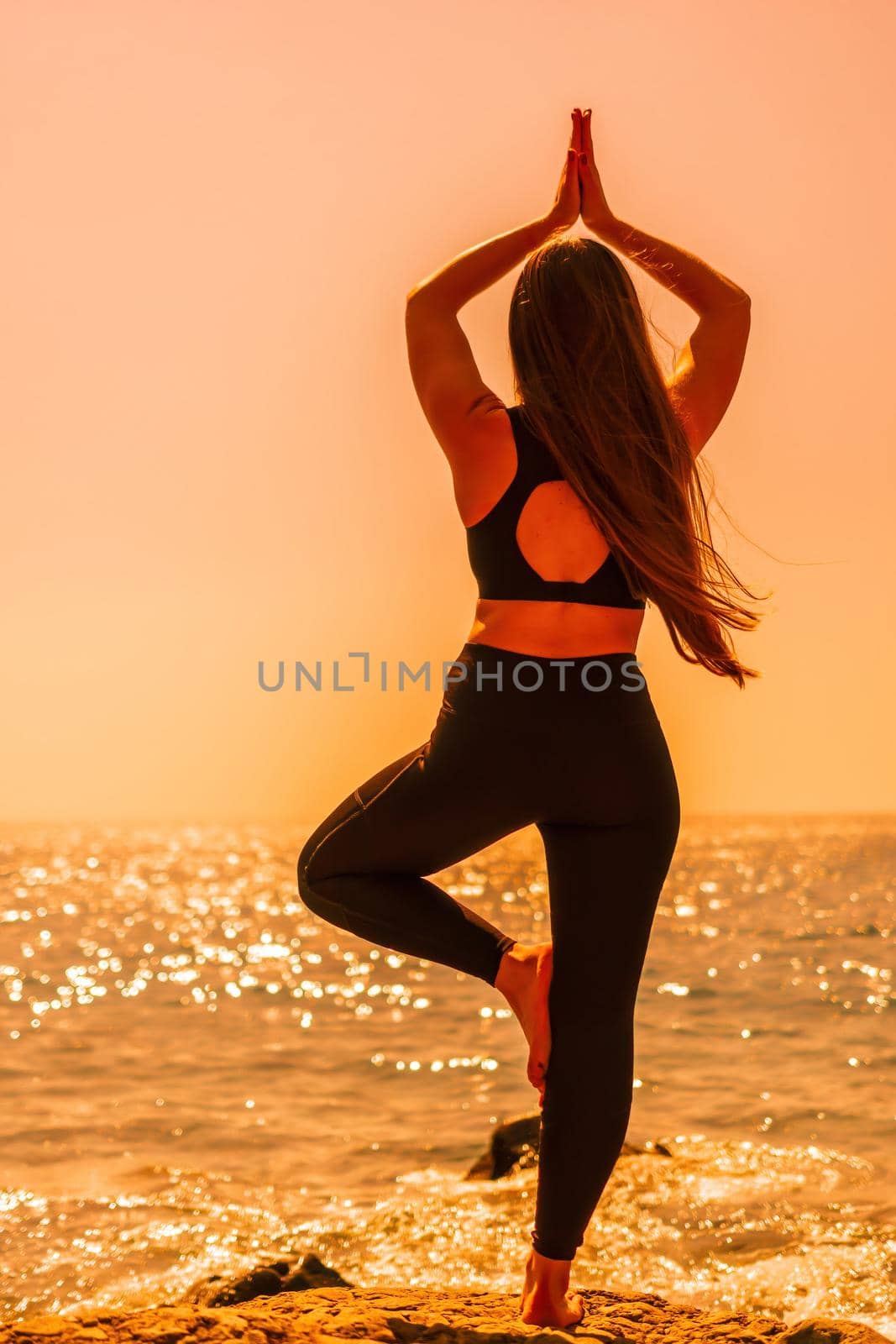 Young woman with long hair, fitness instructor in Sportswear Leggings and Tops, stretching before pilates, on a yoga mat near the sea on a sunny day, female fitness yoga routine concept by panophotograph