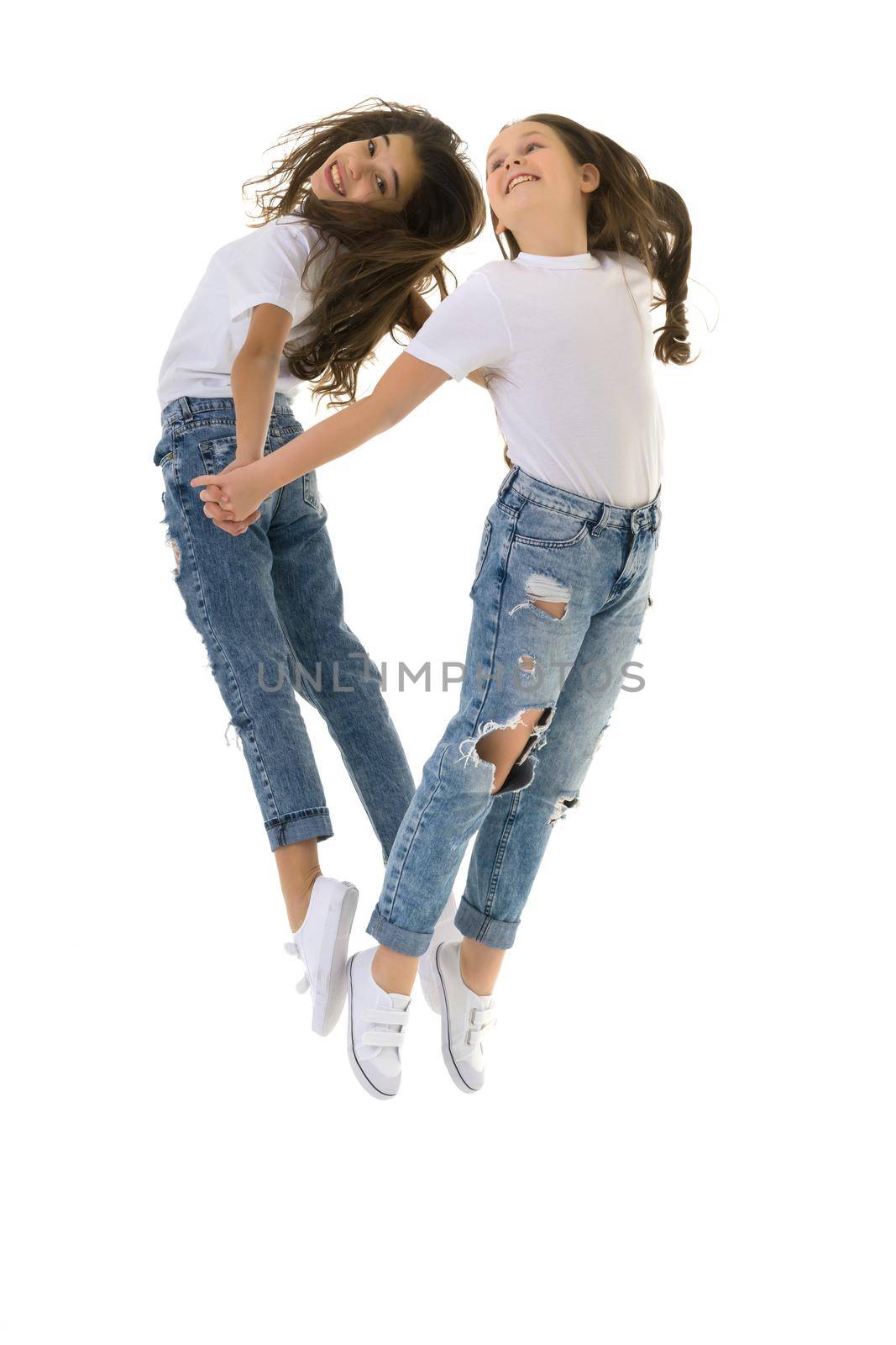 Two cheerful little girls have fun jumping in the studio on a white background.