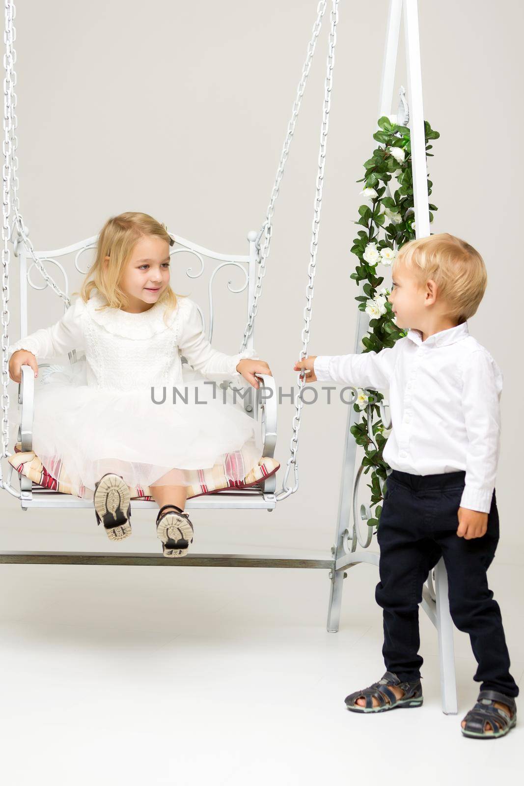 A little boy swinging a swing on which his sister is sitting.