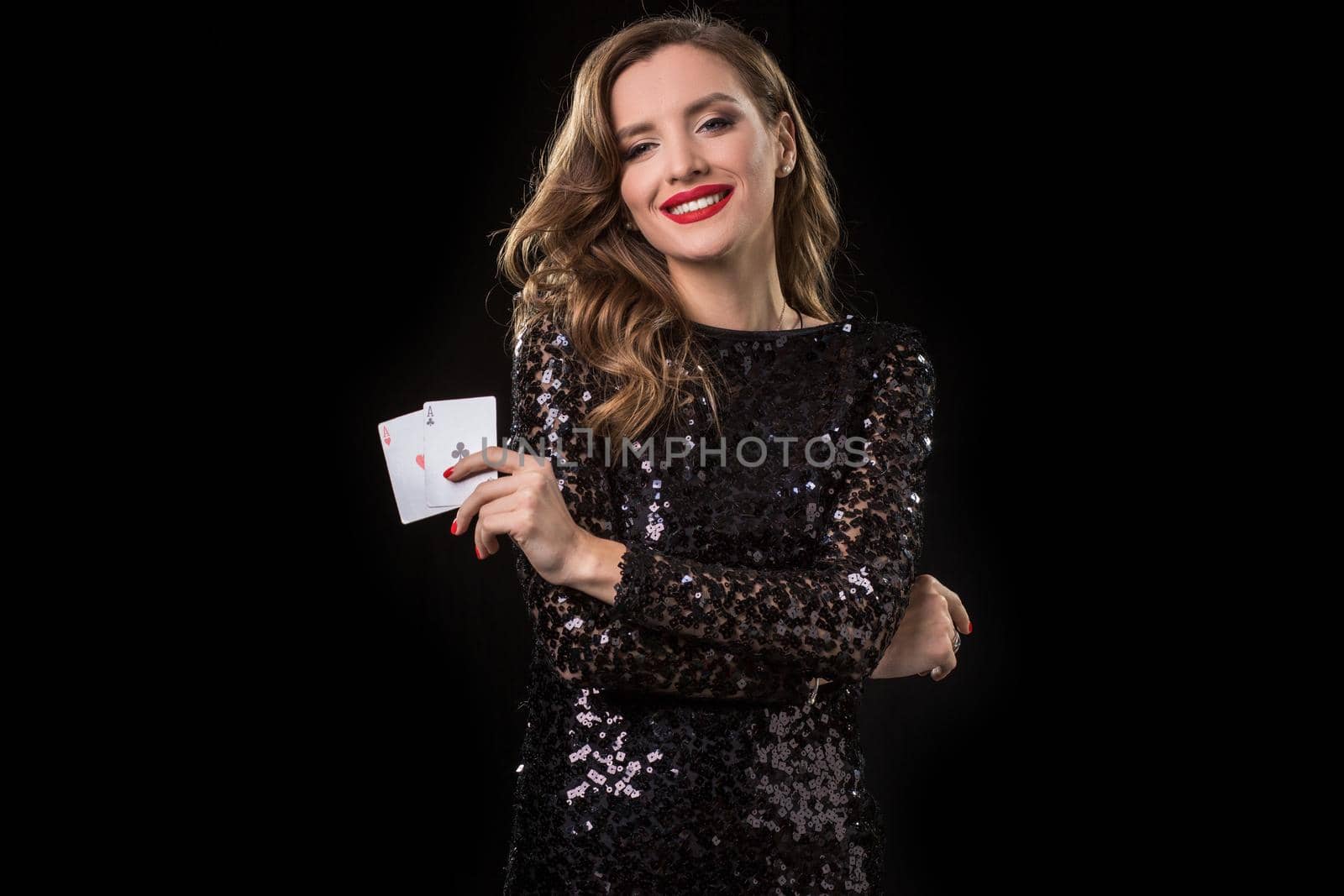 Young beautiful woman in black shiny dress holds poker cards in hands against a black background. The concept of gambling. Casino
