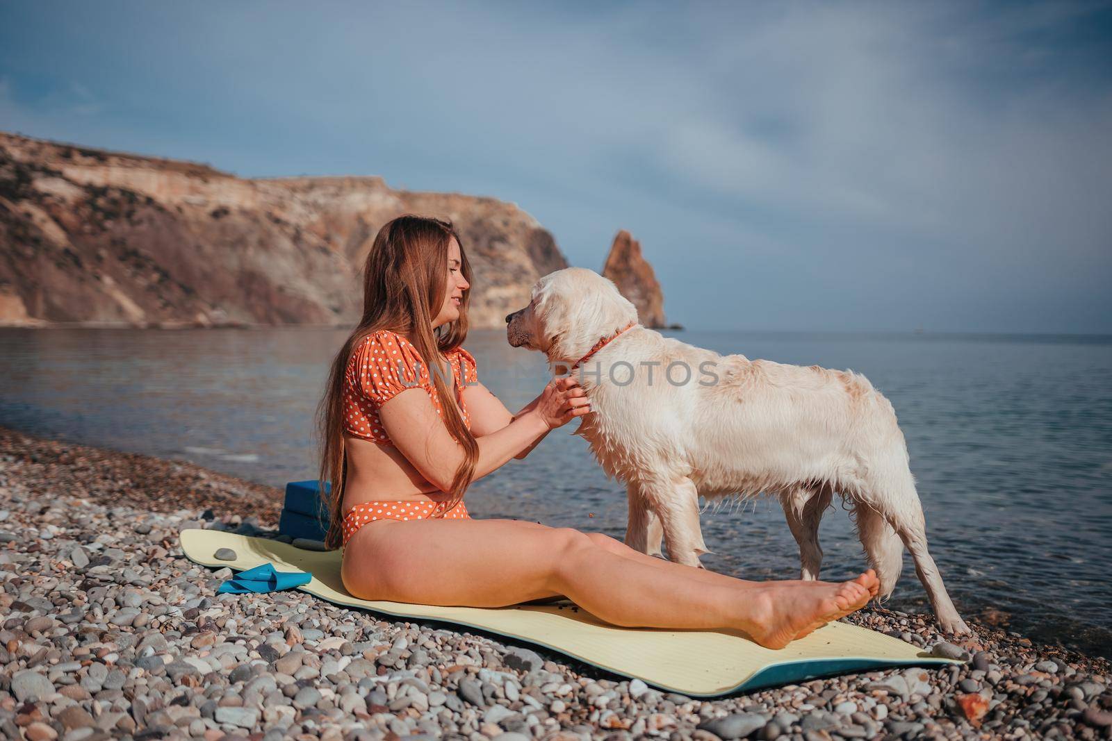 Young woman in swimsuit with long hair practicing stretching outdoors on yoga mat by the sea on a sunny day. Women's yoga fitness pilates routine. Healthy lifestyle, harmony and meditation concept.