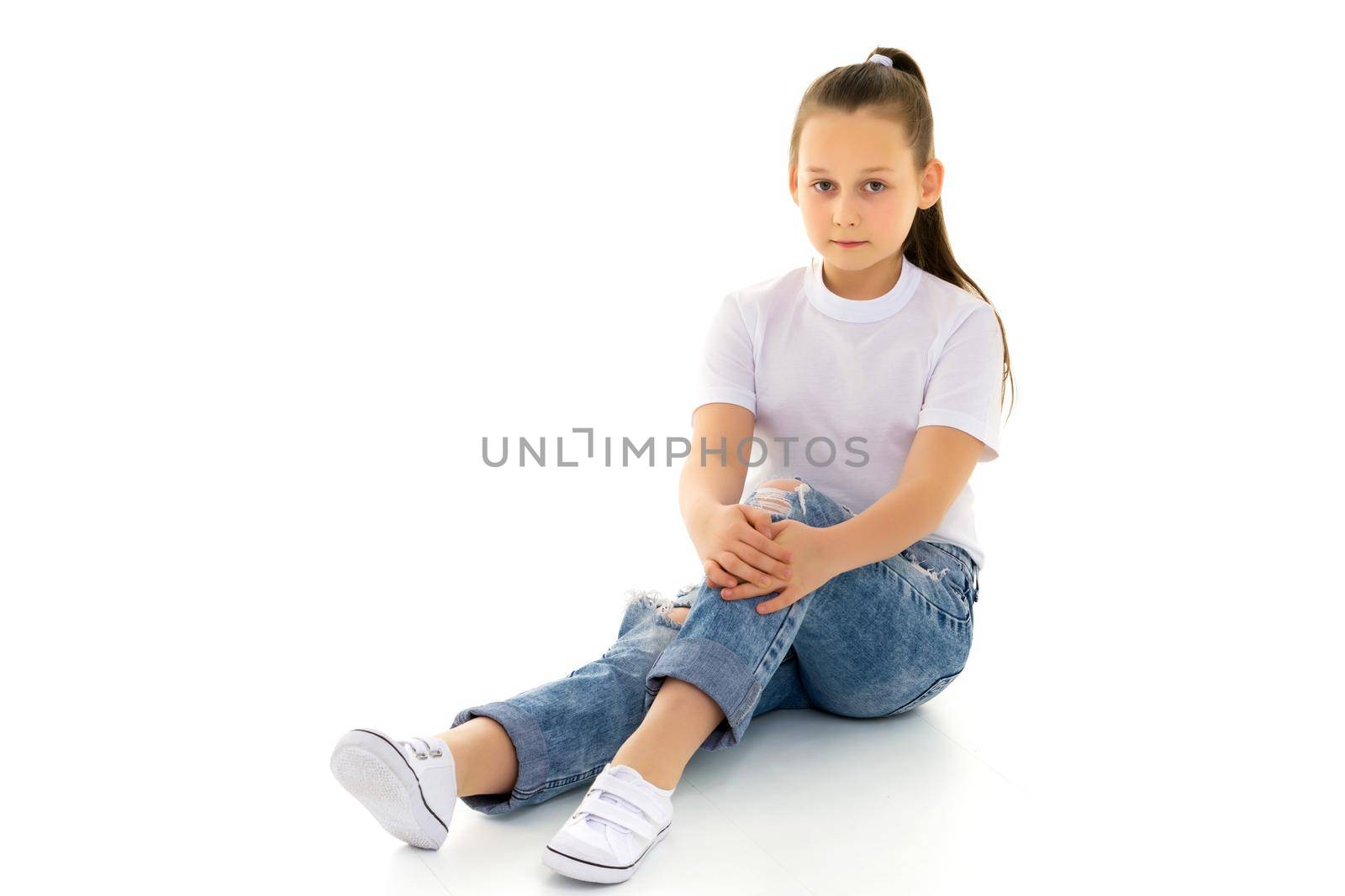 A little girl is sitting on the floor in a clean white T-shirt. by kolesnikov_studio
