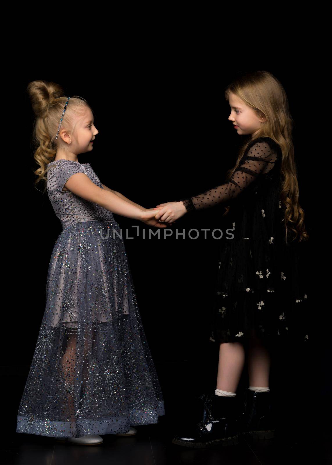 Two little girls hold hands, on a black background. by kolesnikov_studio