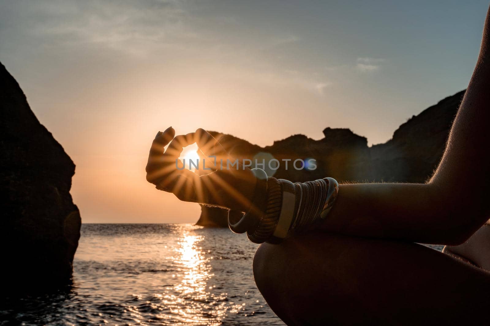 Young woman with long hair in white swimsuit and boho style braclets practicing outdoors on yoga mat by the sea on a sunset. Women's yoga fitness routine. Healthy lifestyle, harmony and meditation by panophotograph