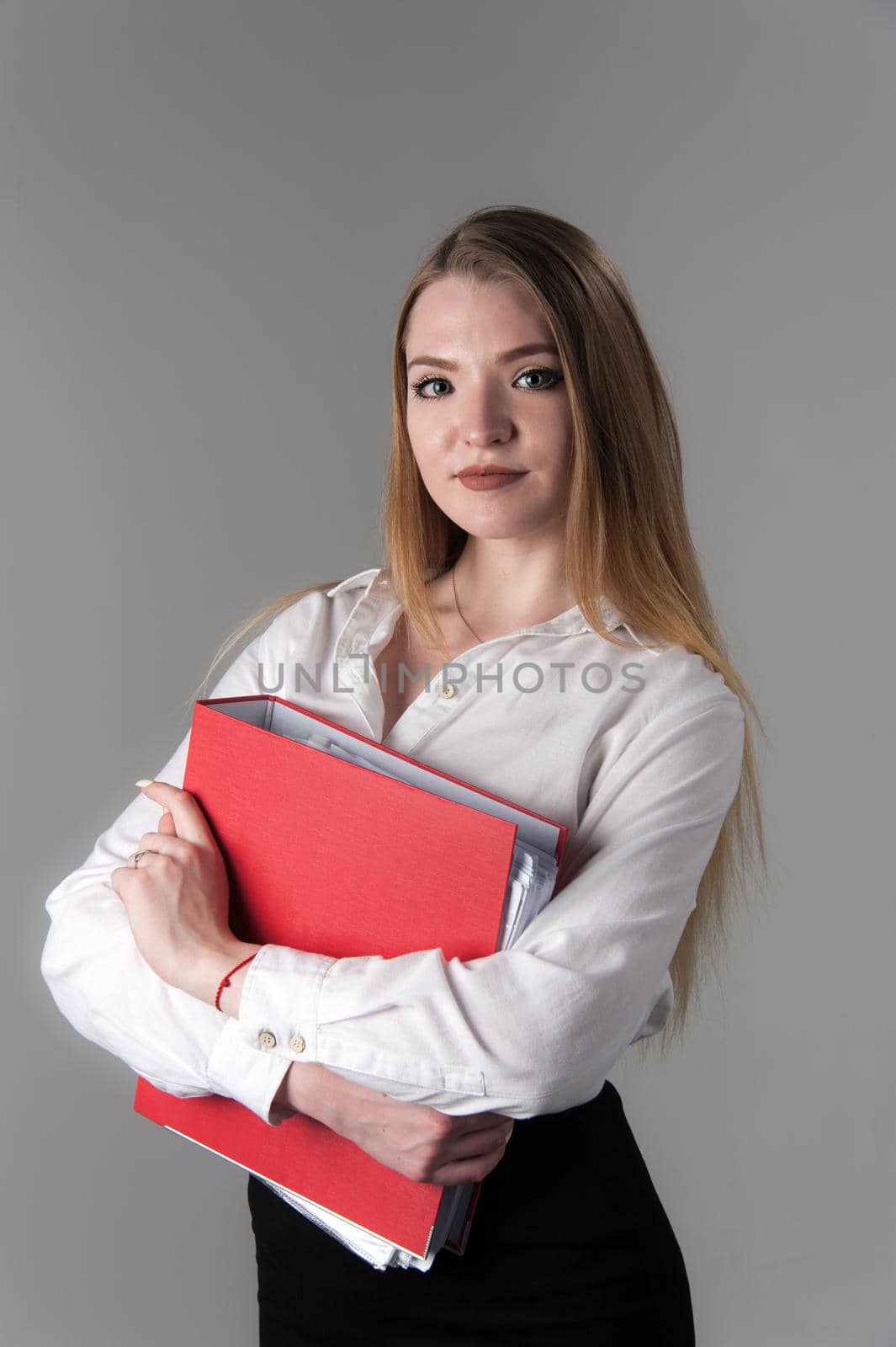 Portrait of a young attractive woman with blond hair on a neutral gray background. Red folder in hand.