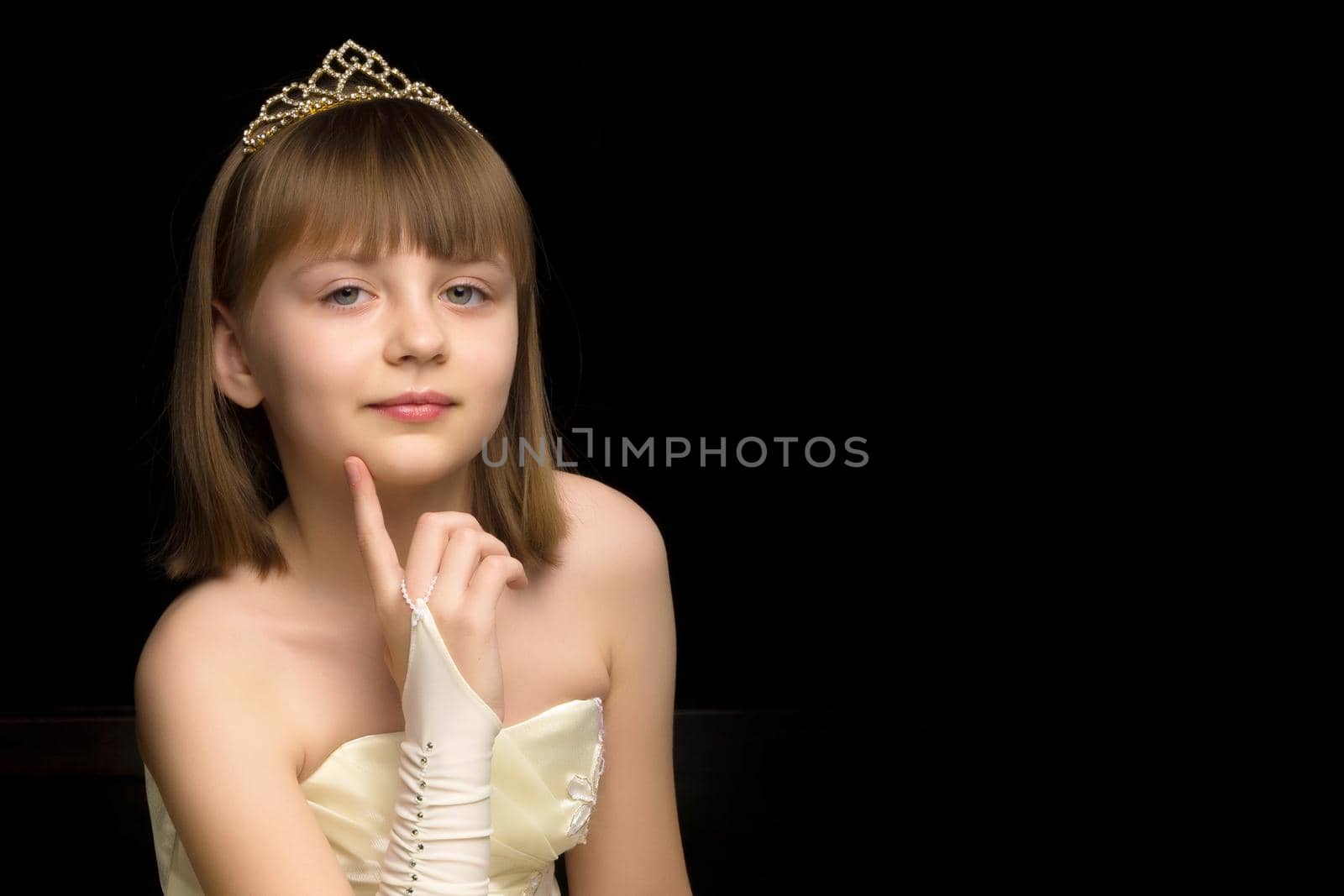 A charming little girl folded her hands around her face. The concept of beauty and fashion, children's emotions. Isolated on a black background.