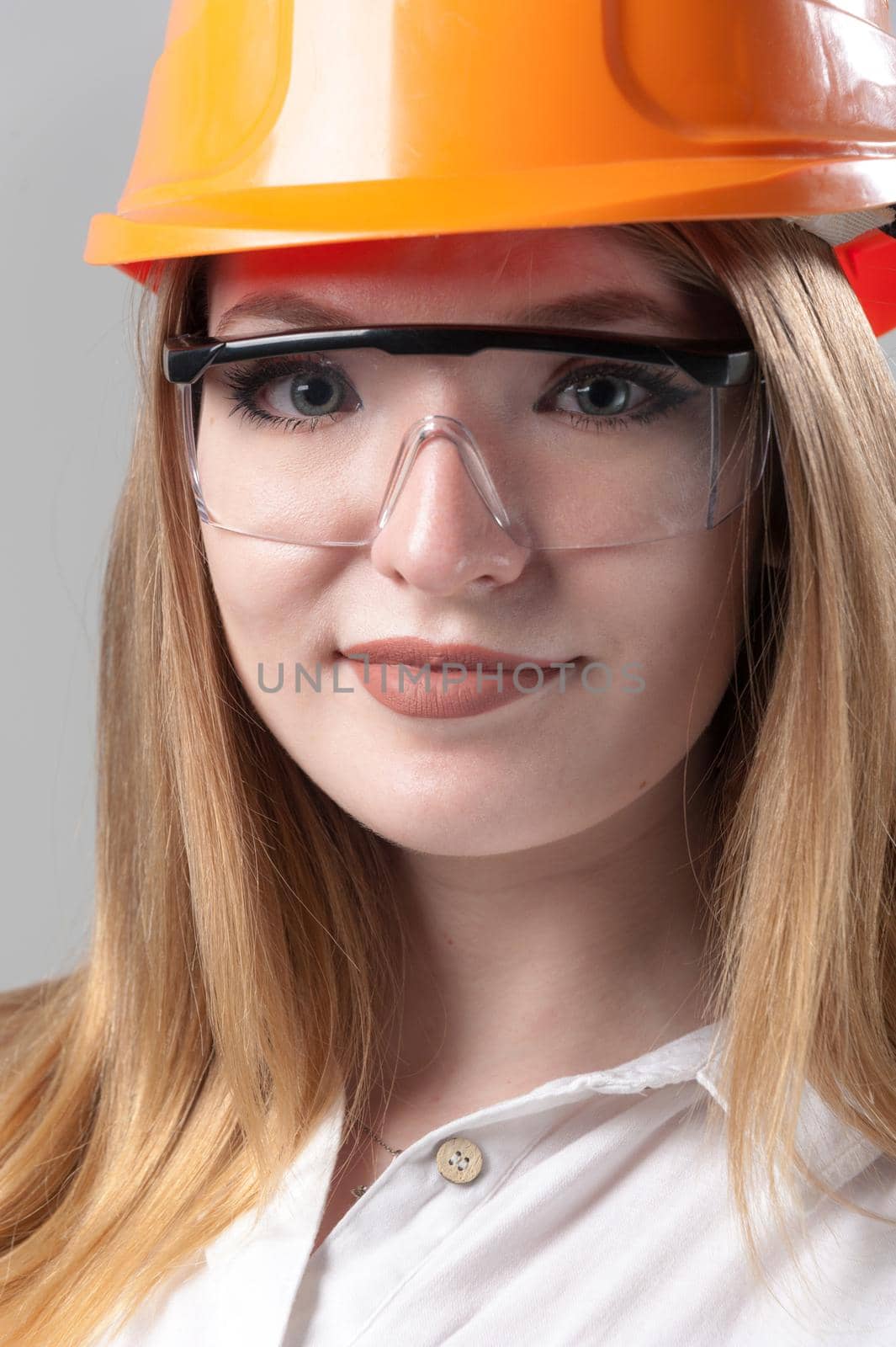 Portrait of a young attractive woman with blond hair in orange helmet on a neutral gray background. by bashta