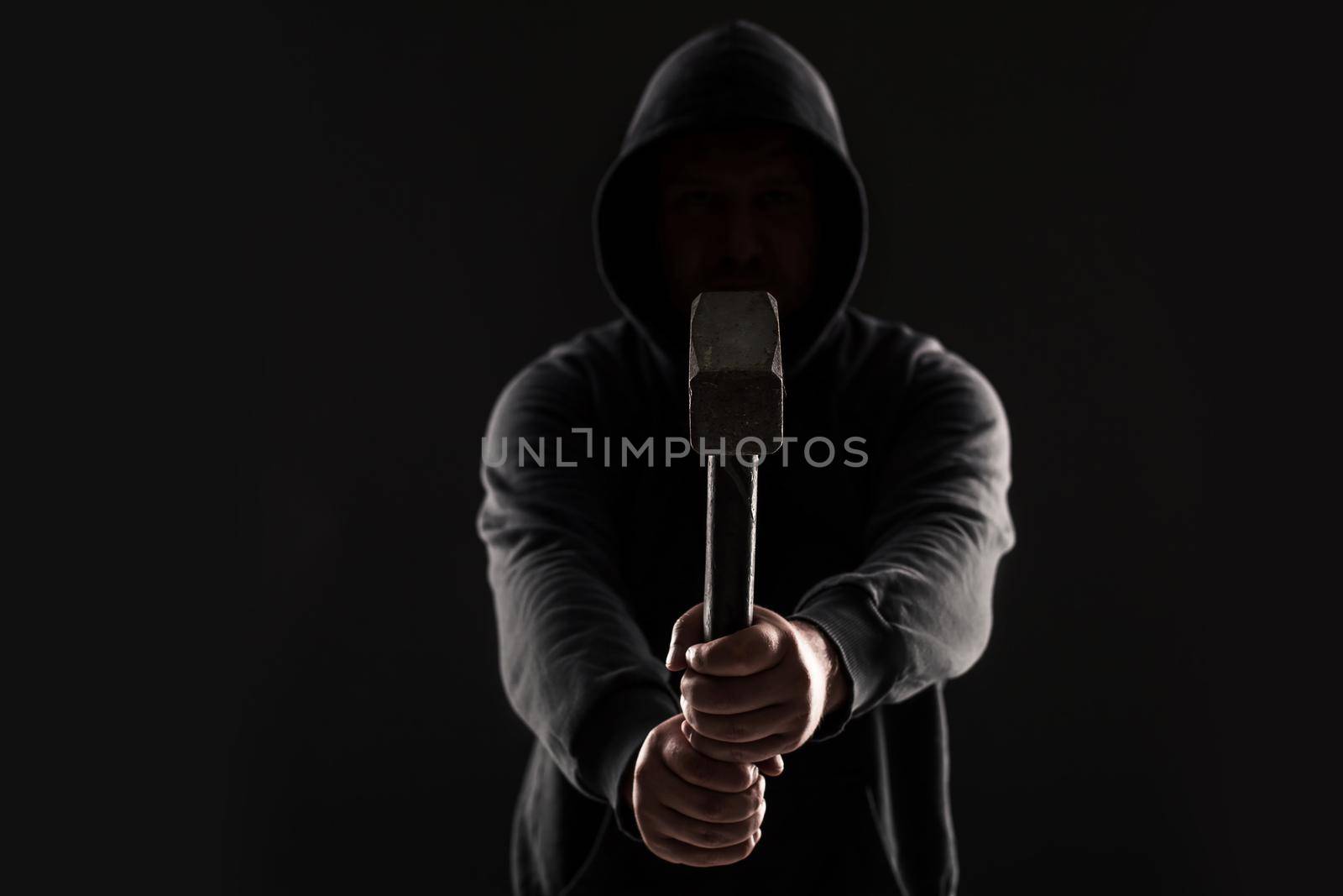 Criminal in dark clothes and balaclava with hammer. On black background at the studio. Bandit and thief