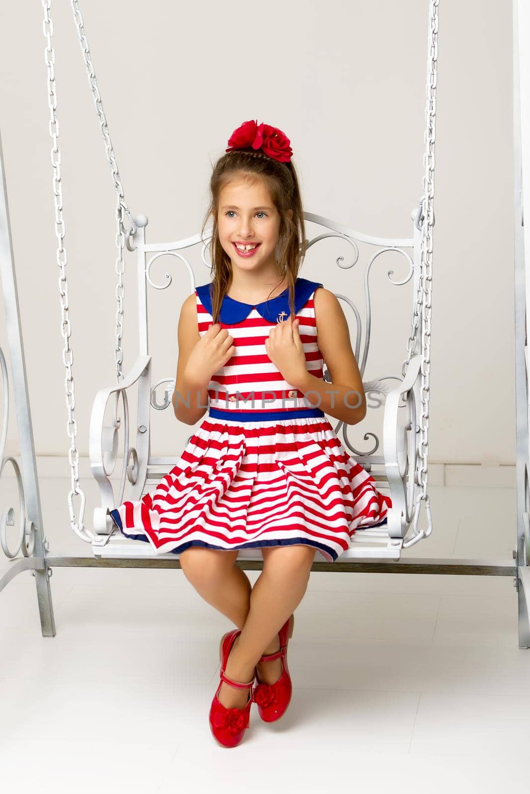 Beautiful little girl swinging in the studio on a swing. Concept of a happy childhood, family well-being.