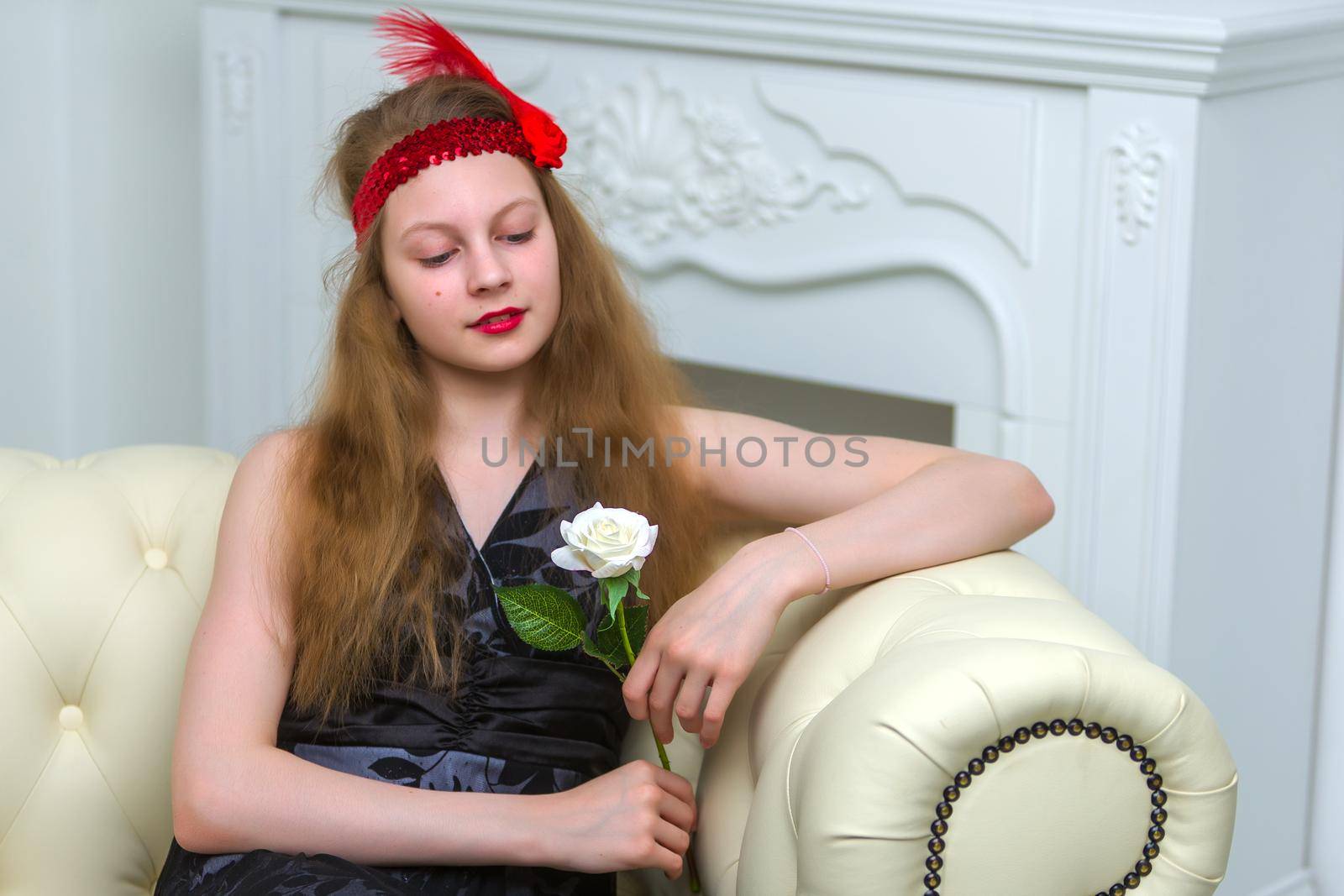 Teen girl sitting on the couch holding a flower in her hand. by kolesnikov_studio