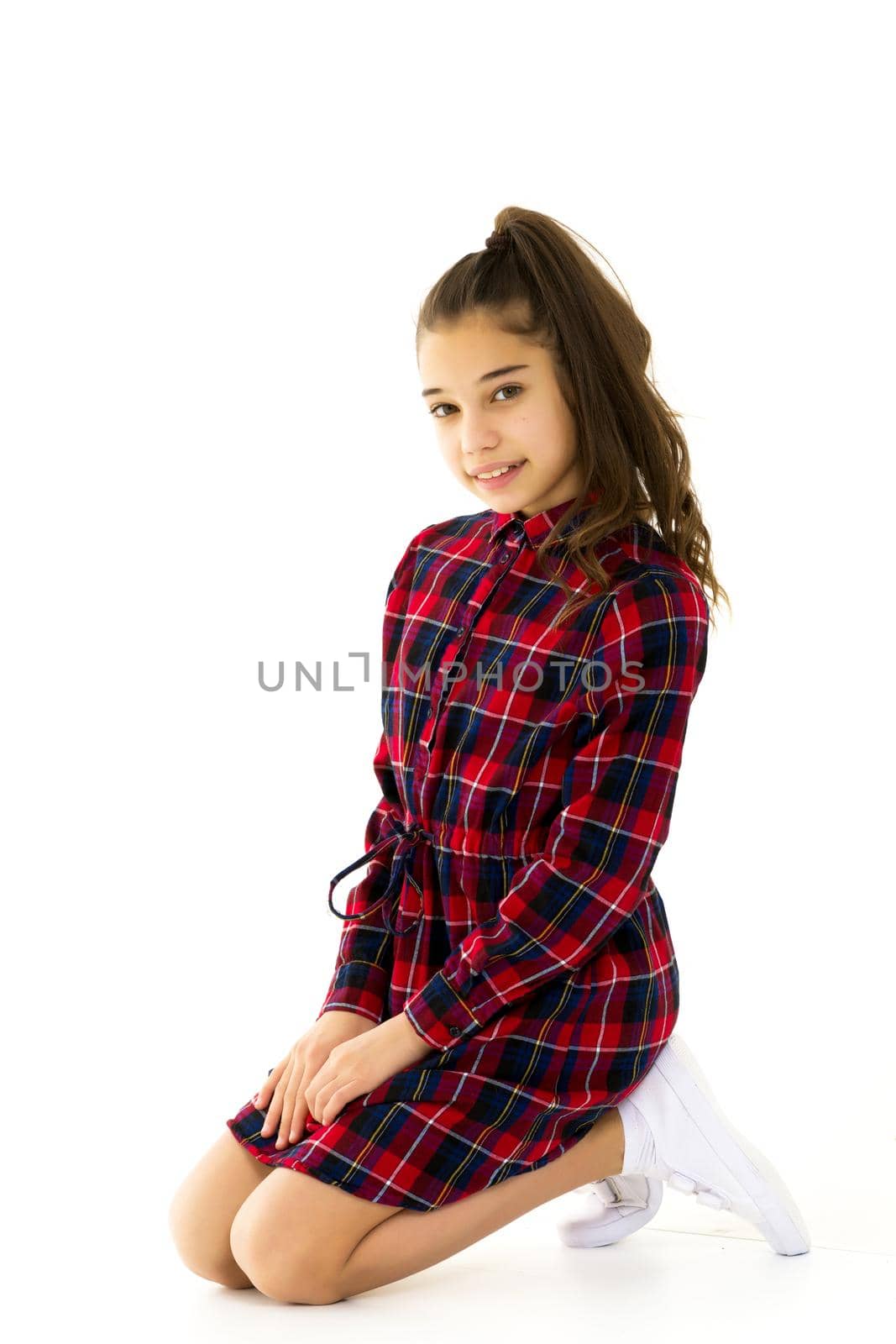 Beautiful little girl kneels in the studio on a white background. The concept of beauty and fashion, children's emotions. Isolated on a white background.