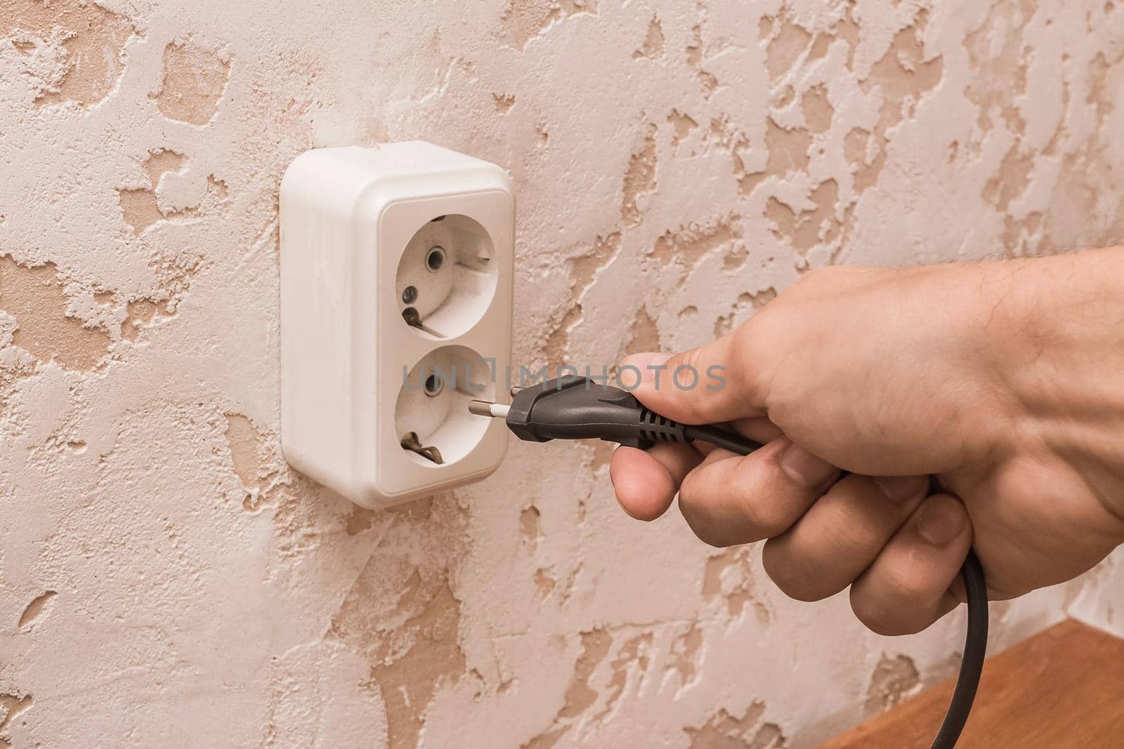 A man hand inserts or removes a plug from an outlet in a modern interior. Safe use of electrical appliances concept by AYDO8