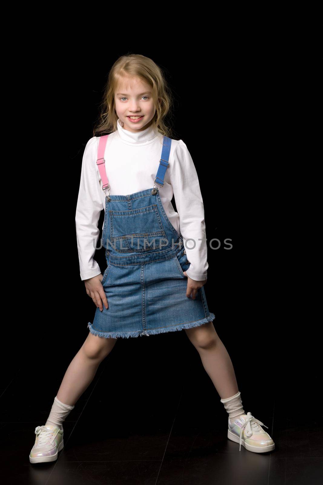 Beautiful little girl in a short denim dress. Concept of beauty and fashion, happy childhood. Isolated.