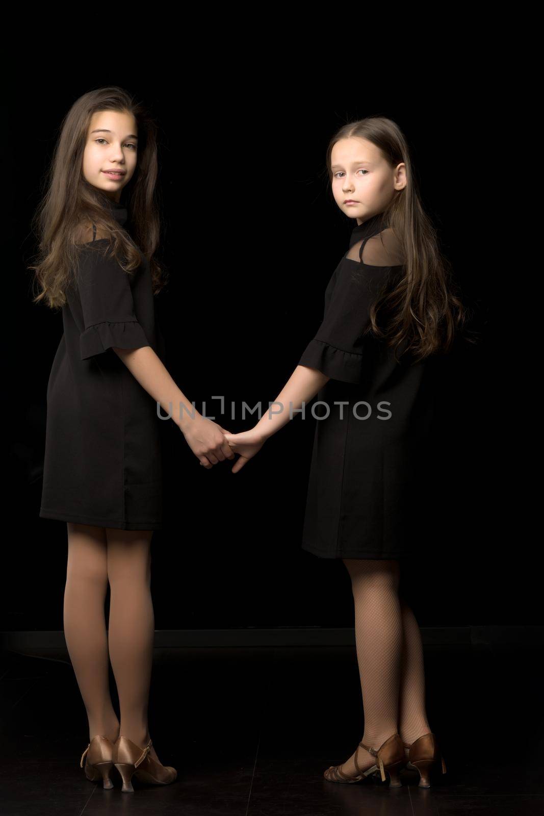Two cute little girls are holding hands. Studio photography on a black background.