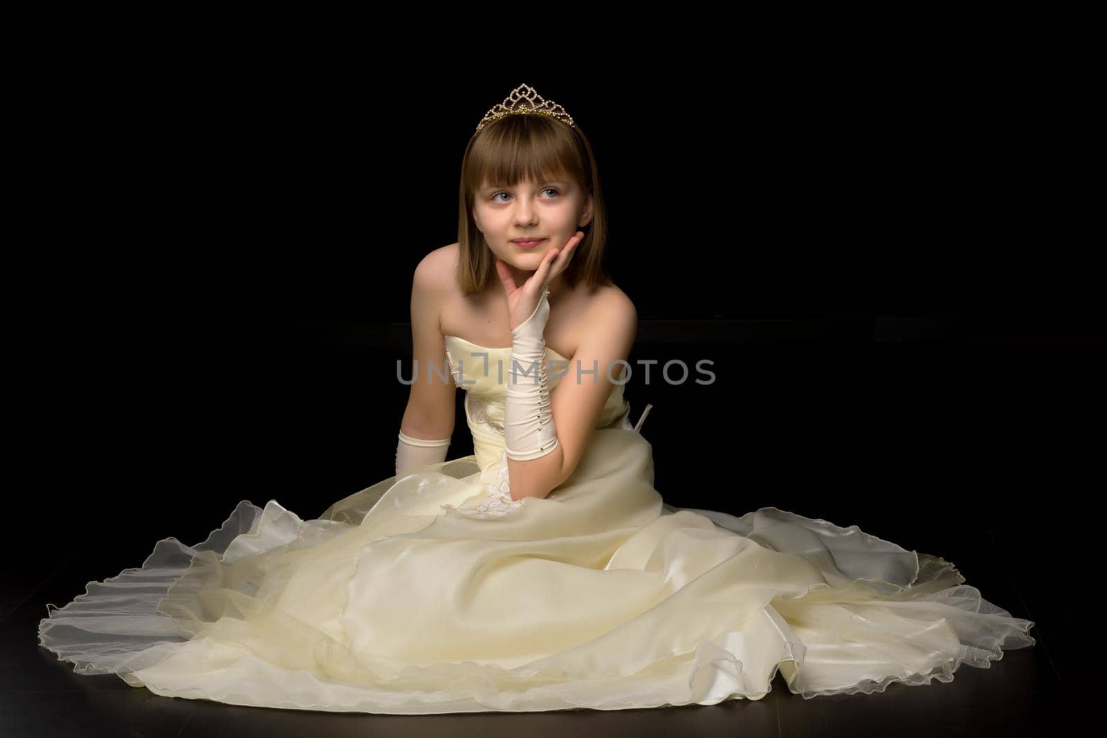 Beautiful little girl sitting in the studio on the floor on a black background. The concept of style and fashion.